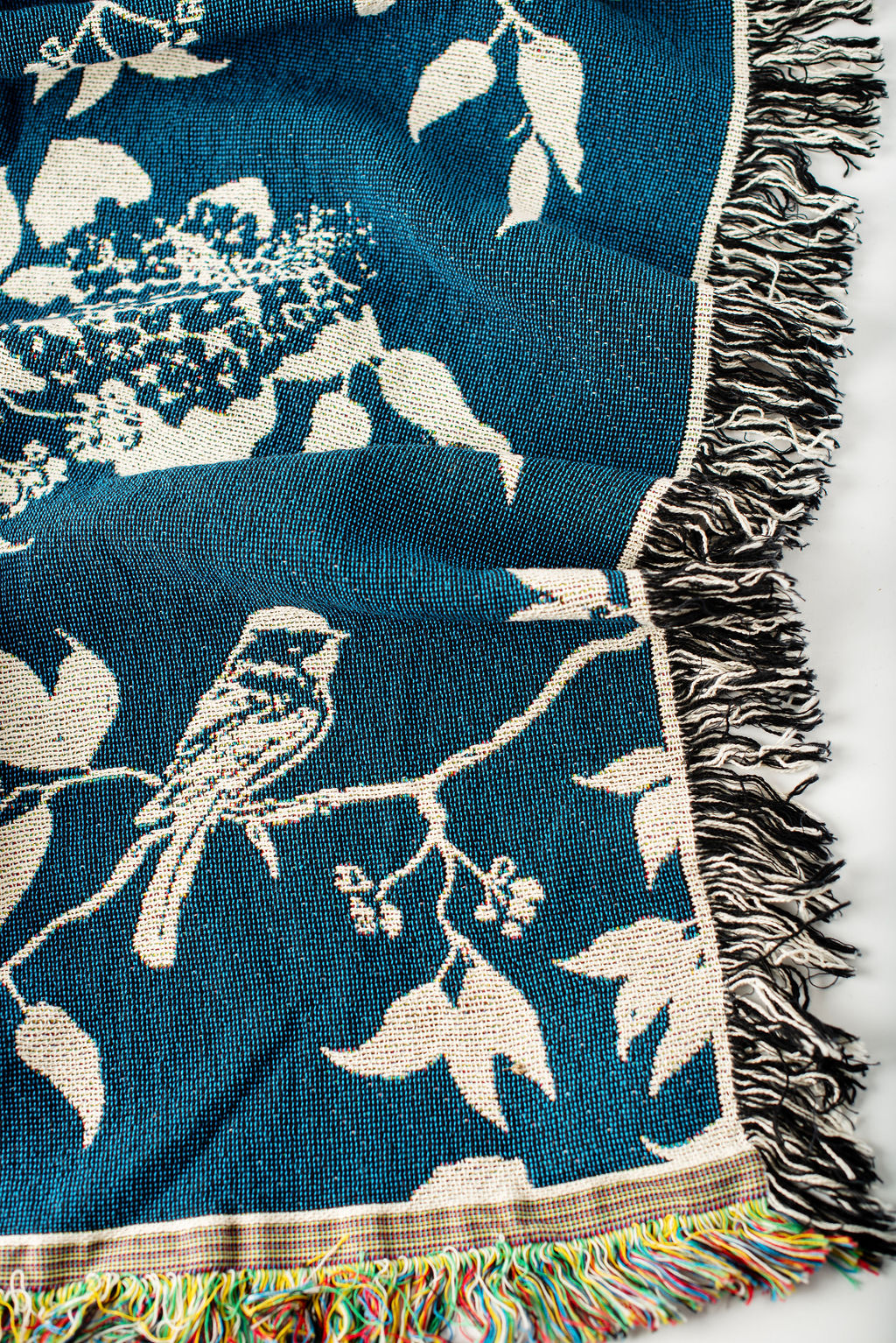 Close-up of Wren Tidesong teal and cream bird and botanical jacquard woven cotton blanket with fringe