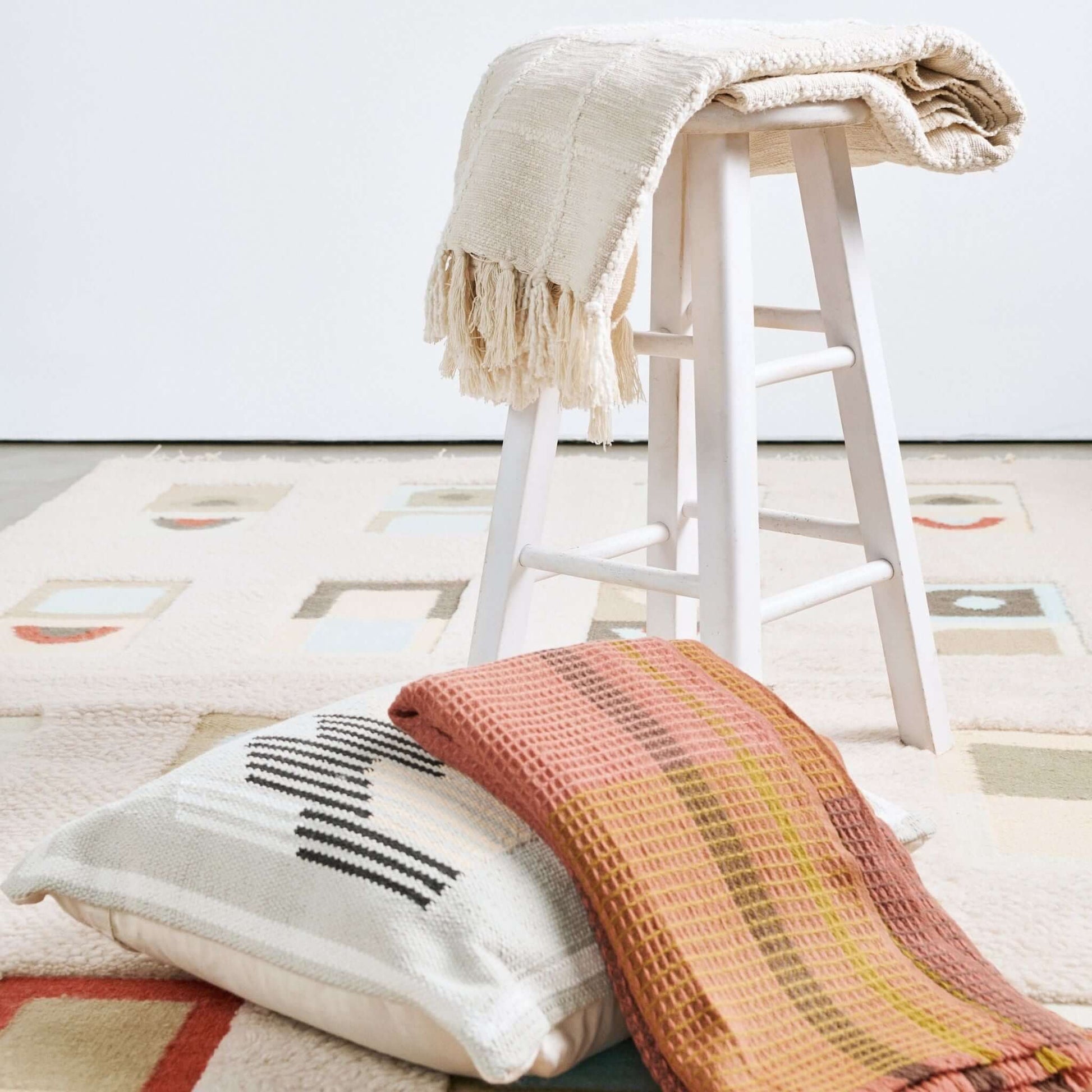 Sea Shell White Textured Checks Handloom Throw draped over a stool with decorative pillows on a patterned rug.