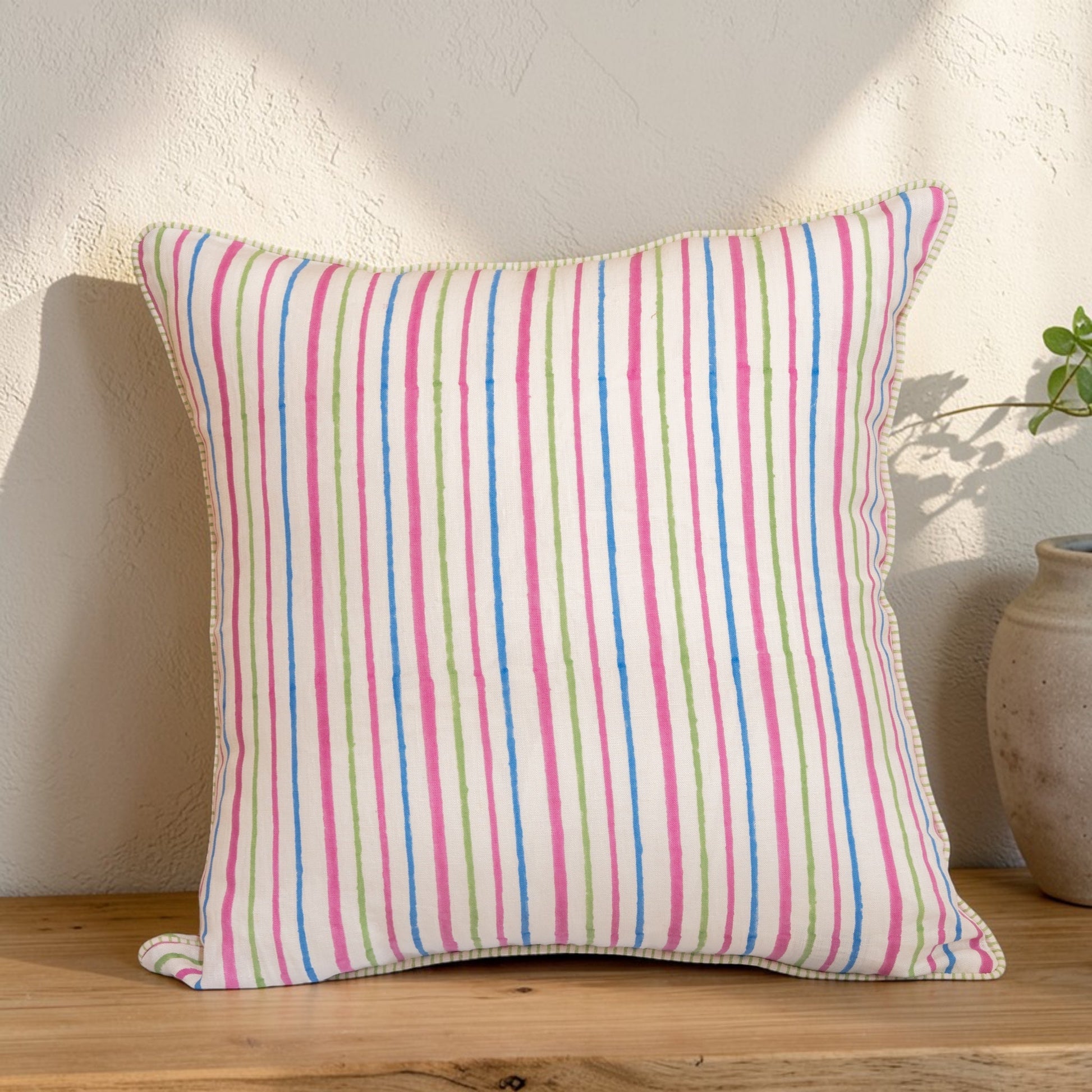 Striped with pink, blue, and green lines hand block printed linen pillow cover in natural dyes  placed on a wooden surface.