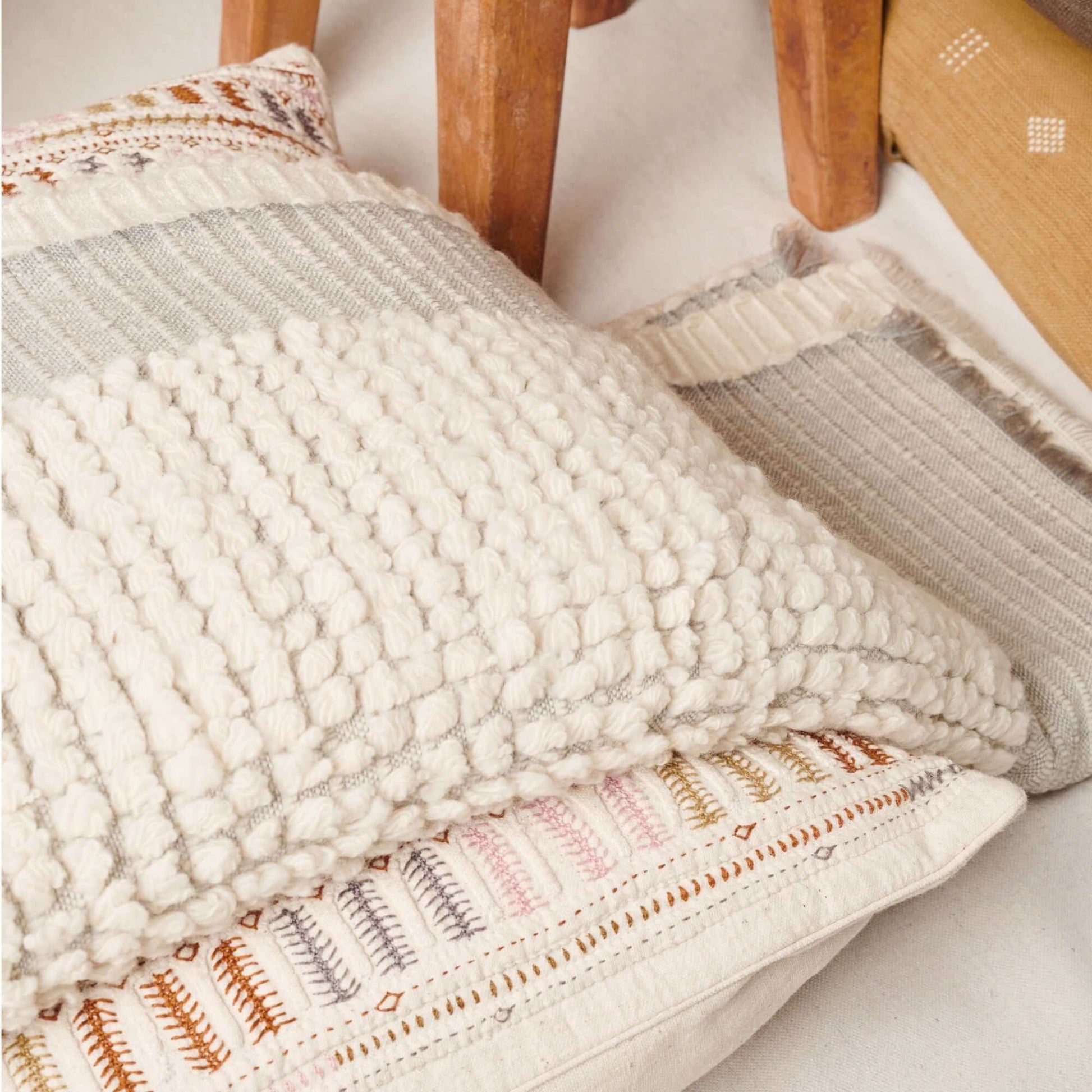 Butterscotch White Handloom Textured Plush Merino Throw draped over decorative pillows on a chair.