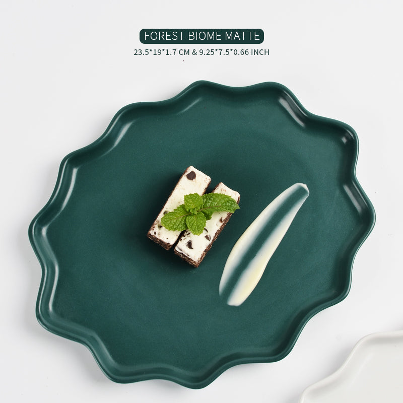 Technical dimension graphic for the BosilunLife Forest Star dinner plate in 'FOREST BIOME MATTE' deep green recycled eco-clay. The plate features a unique, scalloped wavy rim and is elegantly styled with two slices of mint chocolate chip cake garnished with a fresh mint leaf and a cream smear. Text at the top details the size: 23.5 by 19 by 1.7 cm (9.25 by 7.5 by 0.66 inches), showcasing its low-profile, organic oval shape against a white background.