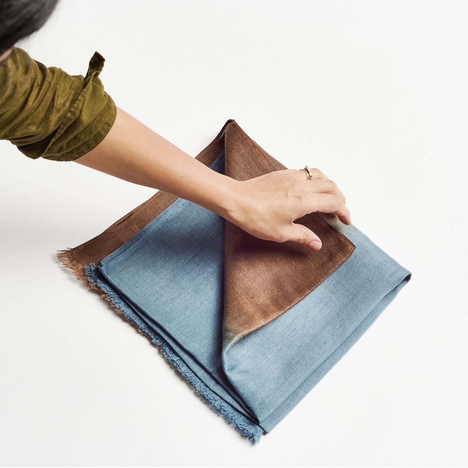 Mahogany Sky Brown Blue Ombre Linen Silk Handloom Scarf being folded by hand to showcase its elegant design.