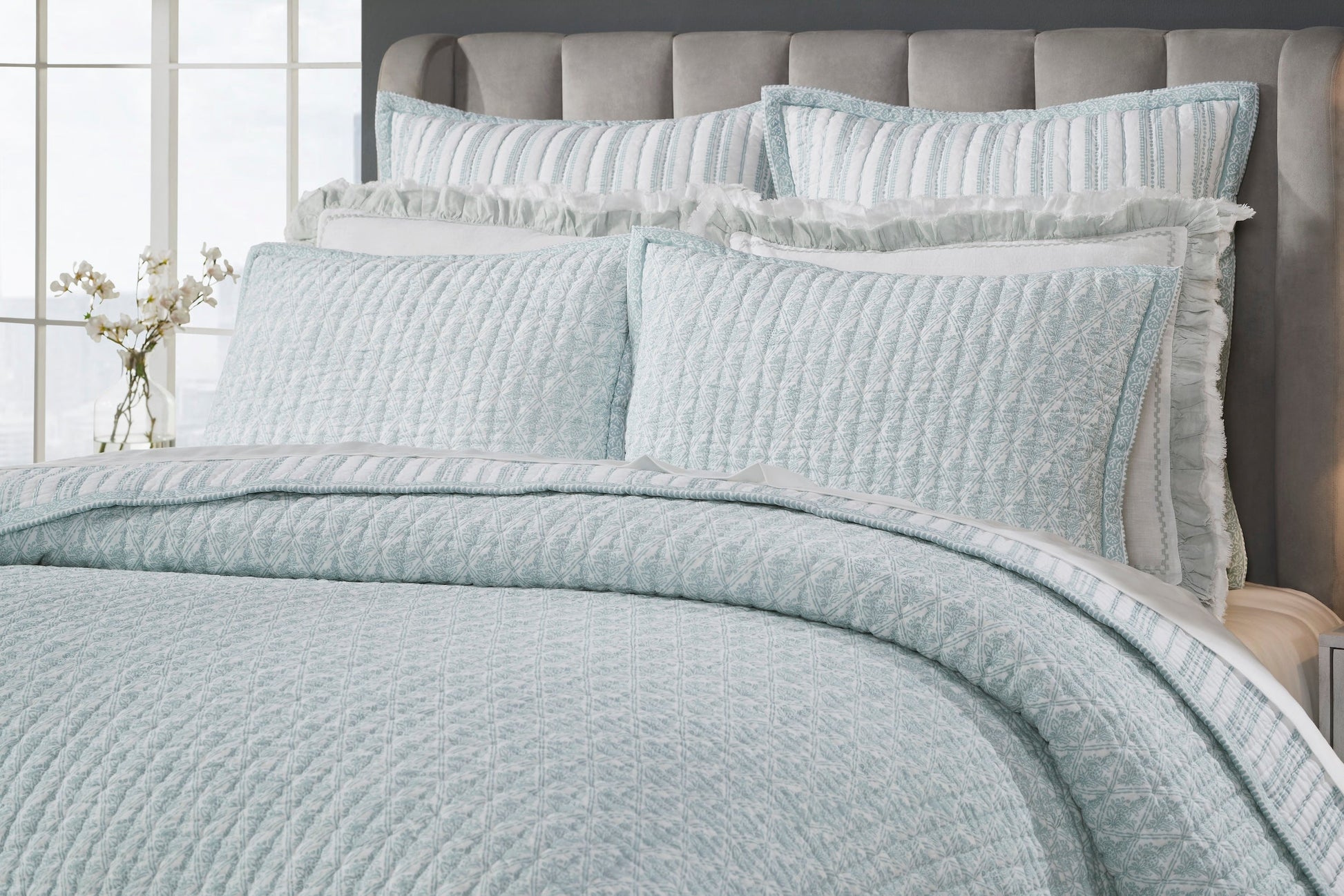 QT-347-11096_3|Close-up of a luxurious blue patterned quilt on a bed, complemented by decorative pillow shams and soft ruffled pillow covers.