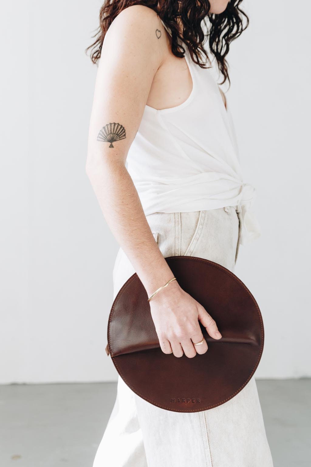 A woman holds a circular dark brown leather clutch in her hands as she walks.