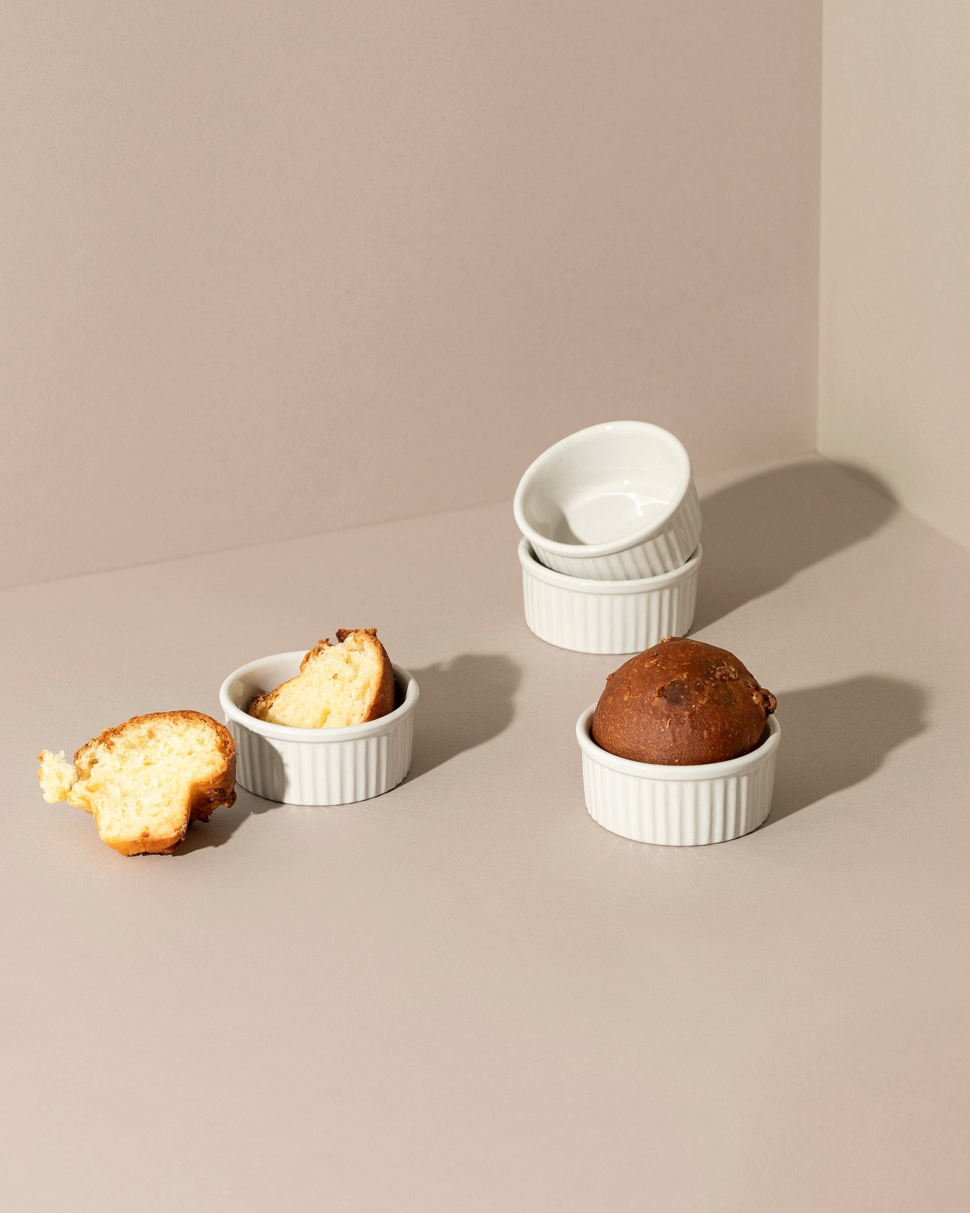 Three stoneware ramekins of varying sizes with lids, displayed on a neutral background. One ramekin contains a baked dessert, possibly a soufflé, and the other two are empty.