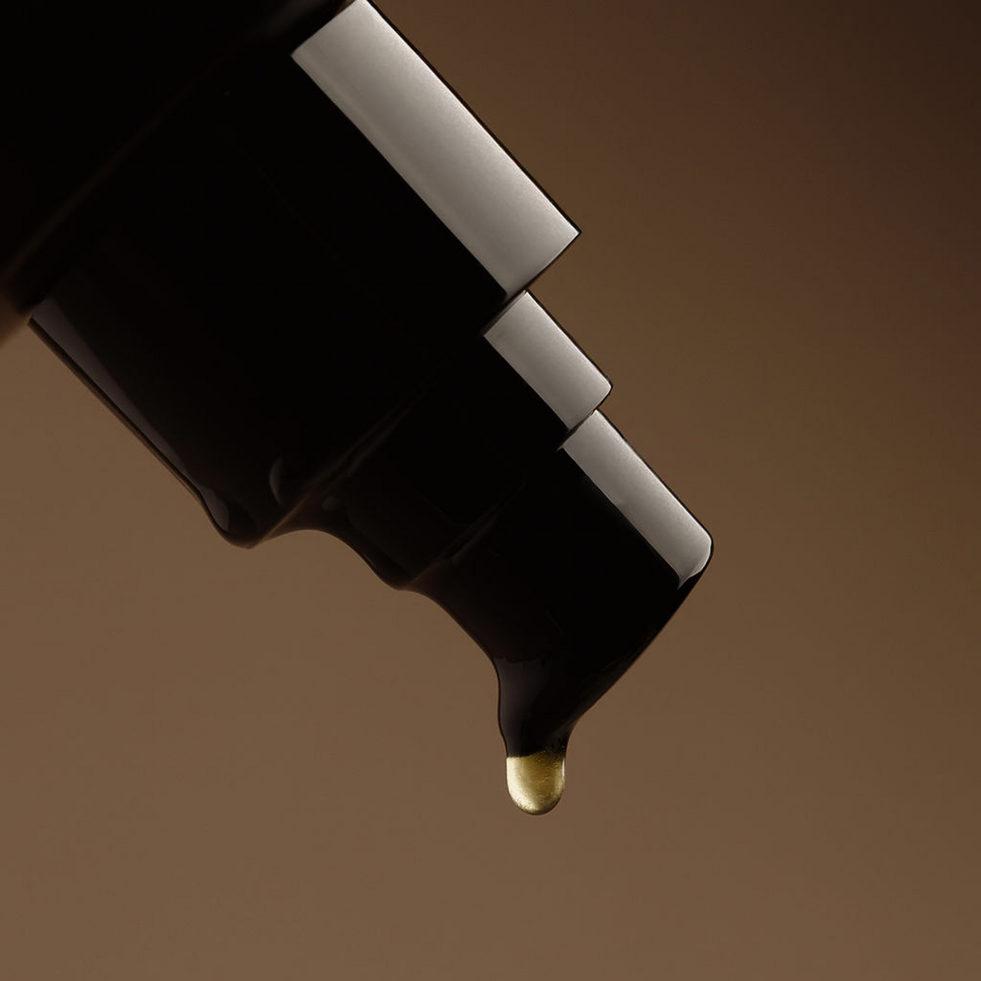 Close-up of a cosmetic applicator with a drop of liquid on a brown background