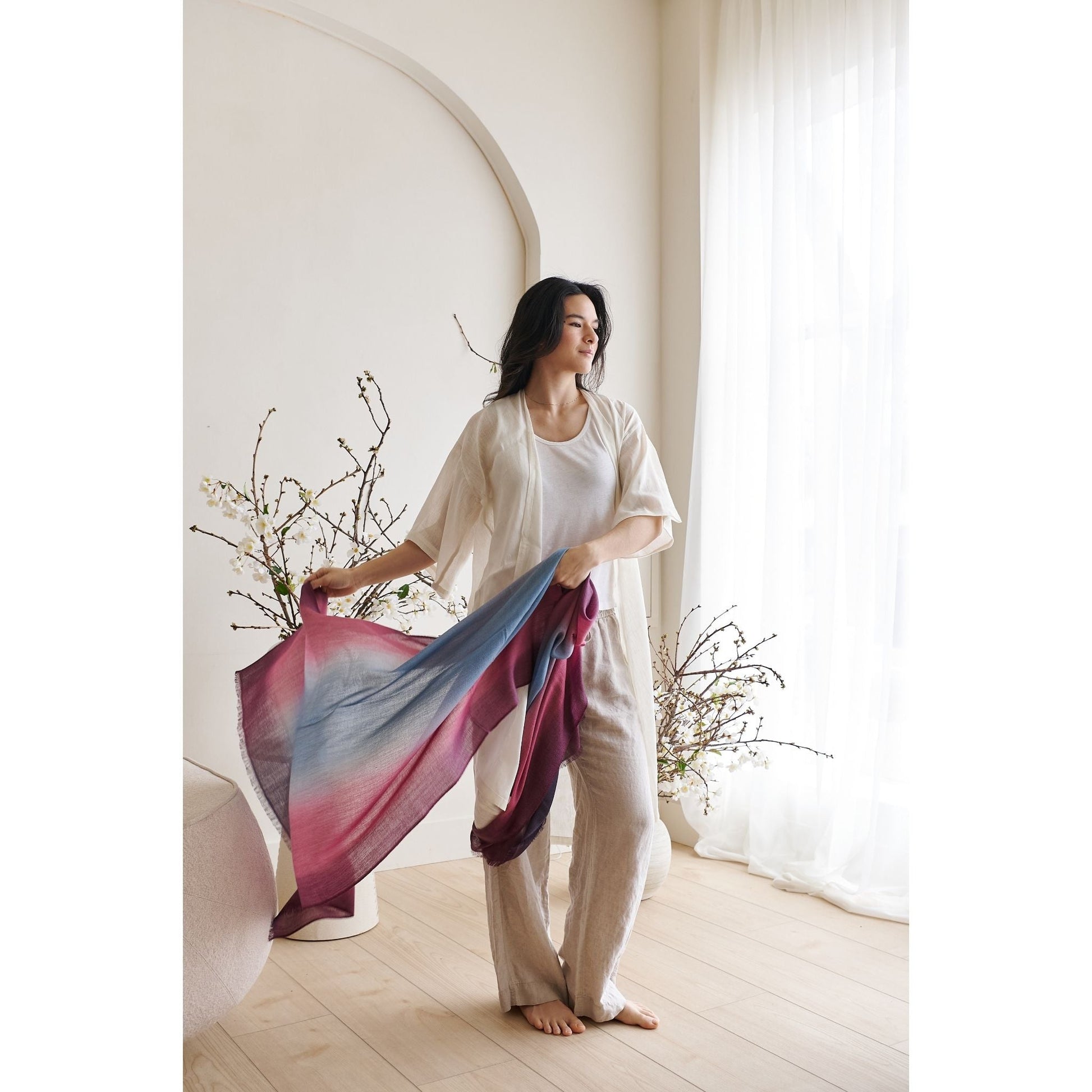 Iris Haze Blue Pink Cashmere Merino Handloom Scarf held by a model in a light-filled room.