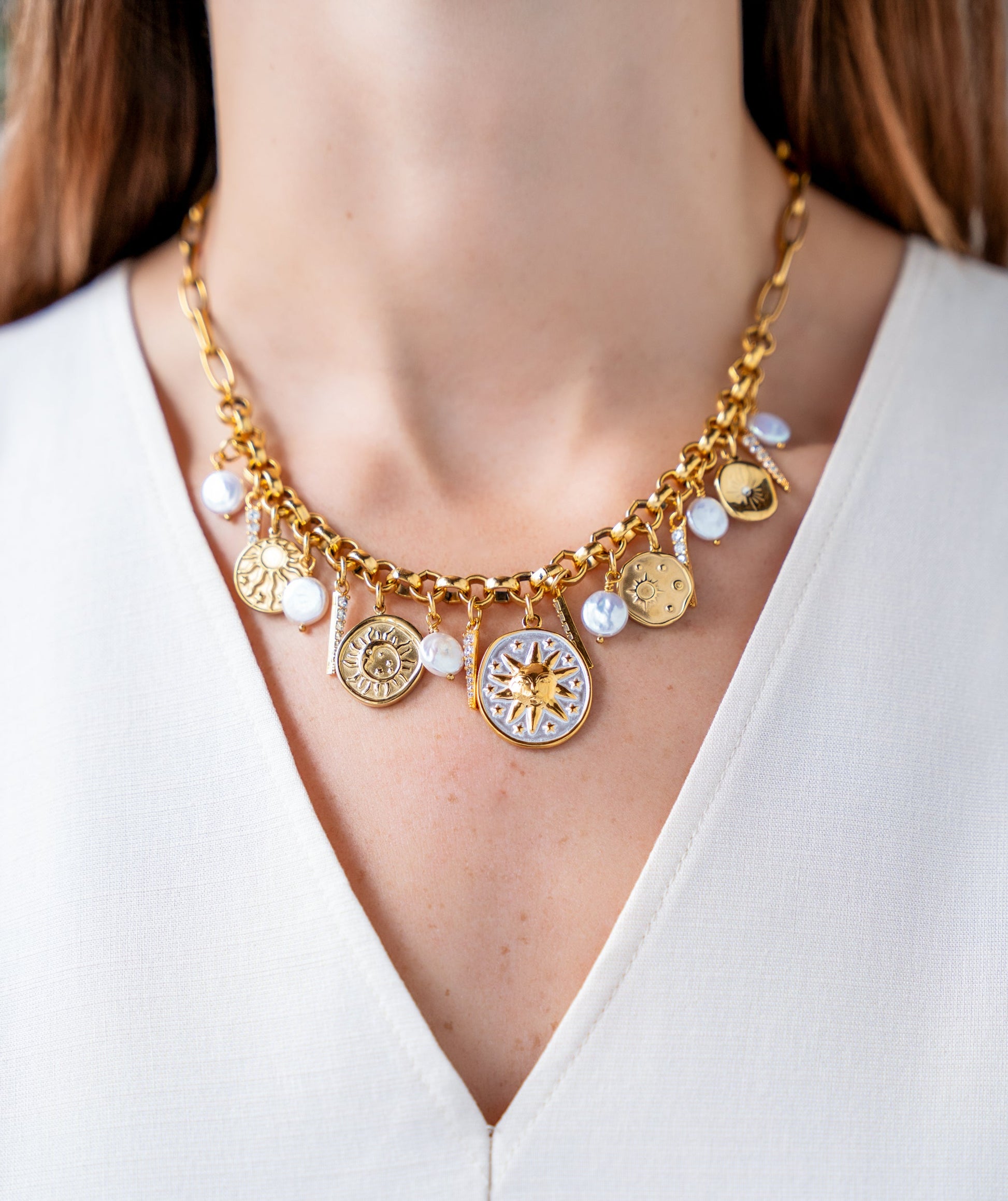 Gold celestial charm necklace with sun medallions, coin pearls, pavé crystal accents, and dangling celestial charms on a chunky chain.