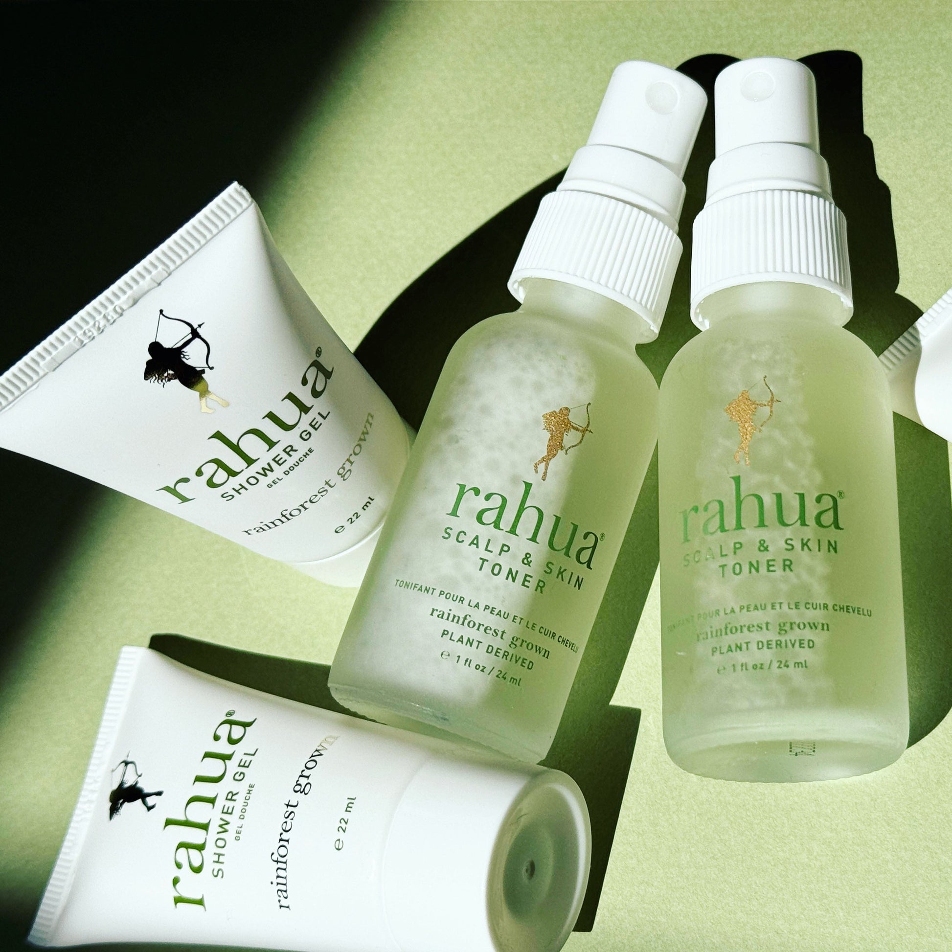 two glass bottles of 2 oz travel friendly tsa safe compliant of rahua scalp and skin toner with two mini tubes of rahua showel gel on a plain green background|variant:1-oz