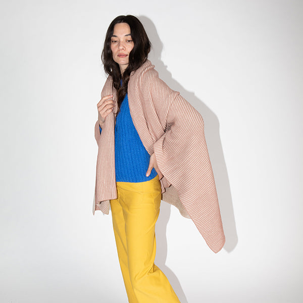 Woman wrapped in a pink textured throw blanket and wearing a blue sweater with bright yellow pants.