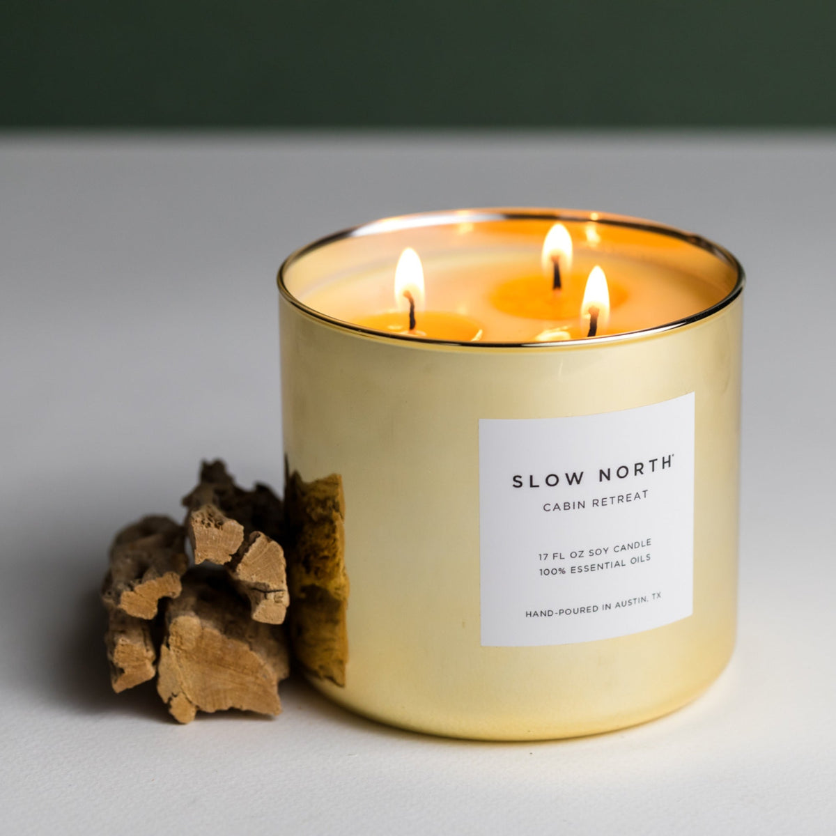 Gold candle with 'Slow North' label and wooden logs on a gray background