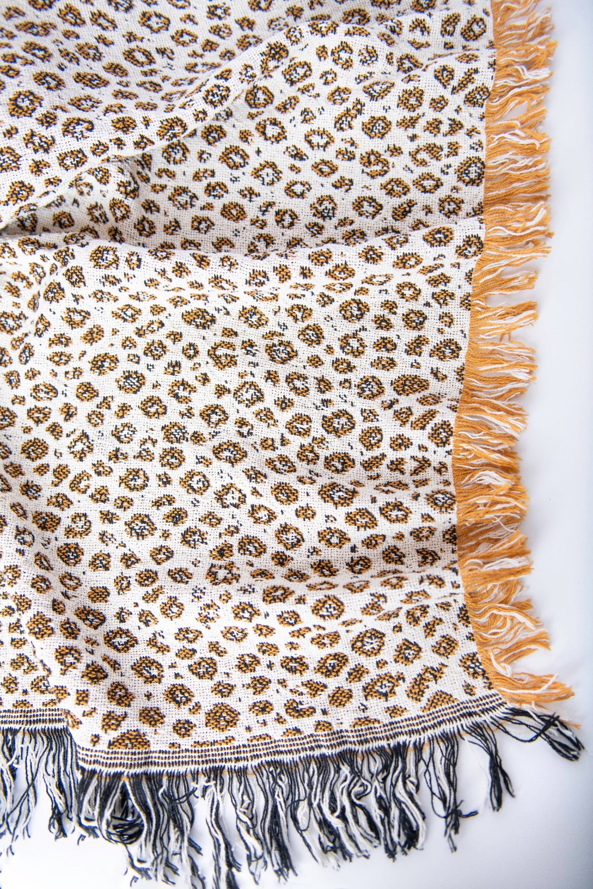 Close-up of Zola golden ochre, black, and cream leopard-print woven cotton throw with fringe