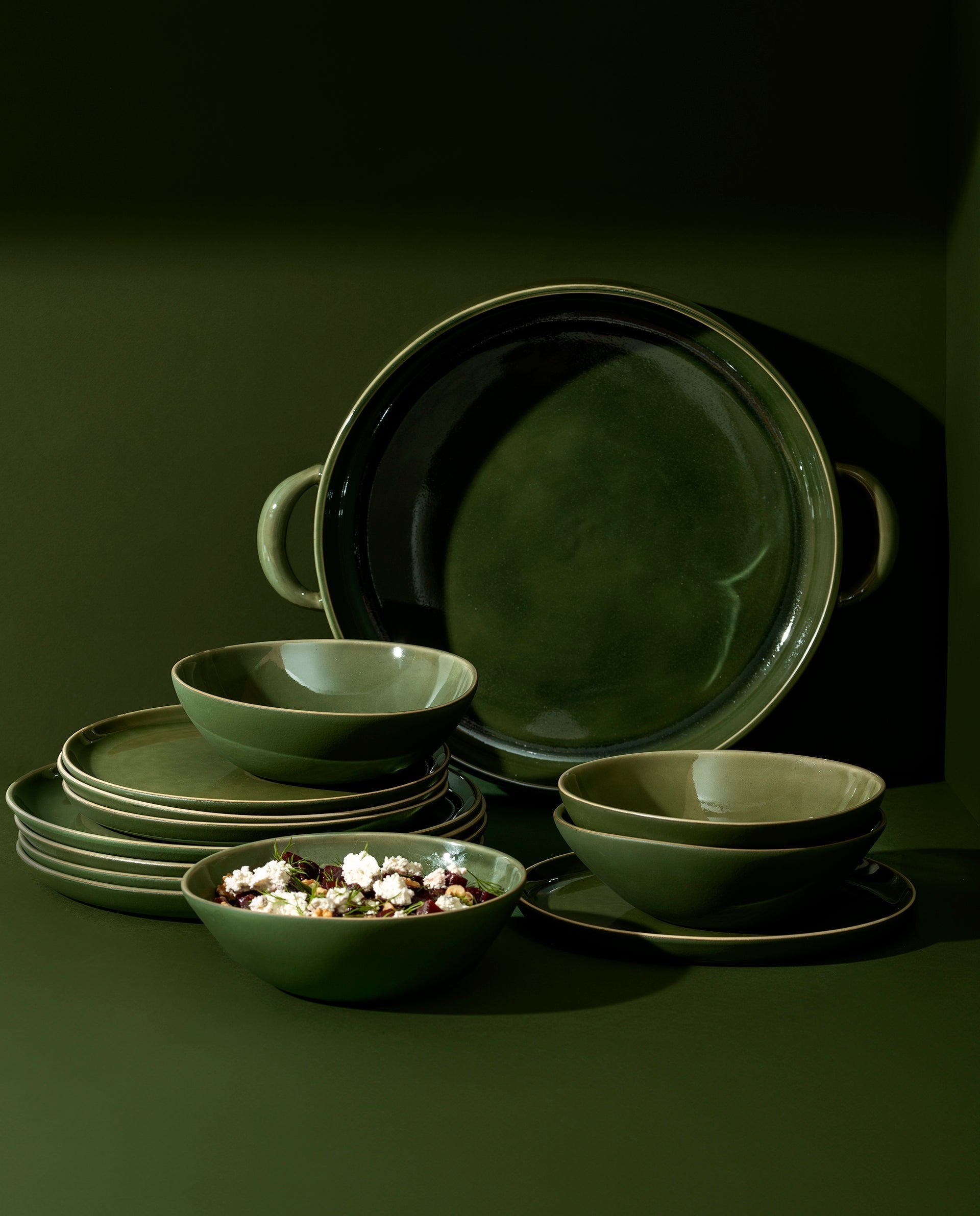 A set of white stoneware dinnerware including flat round dinner plates, flat round salad plates, organic-shaped soup bowls, and a large plate with handles.
