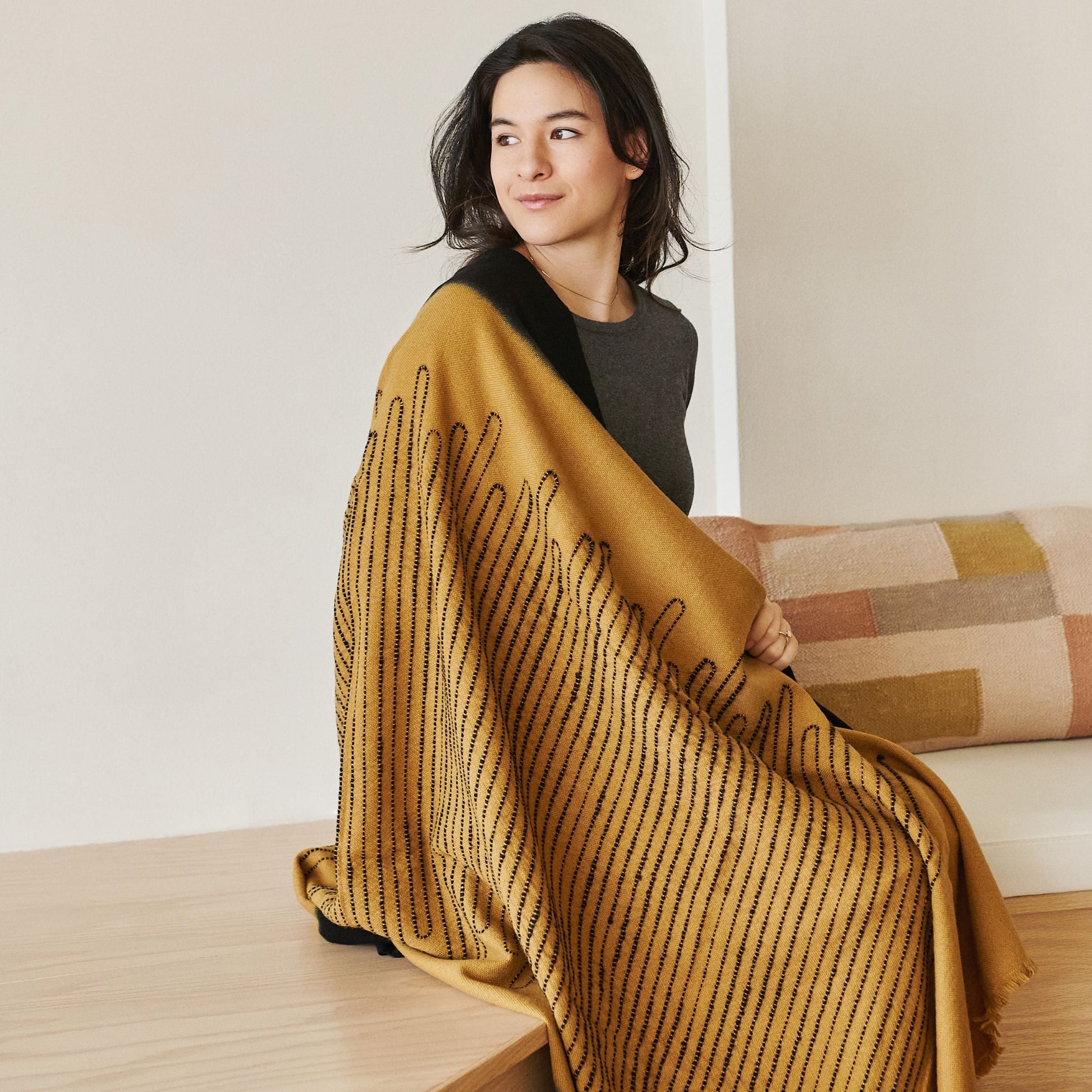 Handwoven Topaz Brown Myrtle Drift Merino Throw elegantly draped over a woman, showcasing its intricate design and texture.