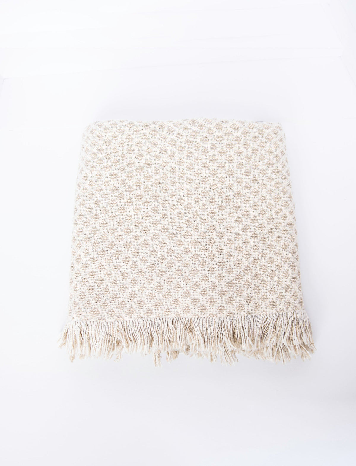 Rowan neutral diamond throw in a stack of colorful Kindly Woven cotton blankets