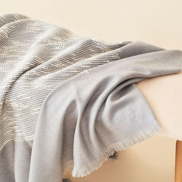 Flo Gray Textured Handloom Merino Throw draped elegantly over a chair, showcasing its luxurious texture and craftsmanship.