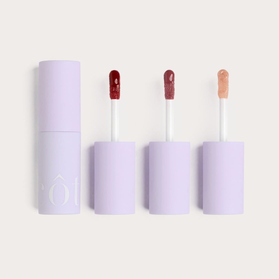 Three lip gloss containers with their respective applicators displayed side by side, with the central container slightly advanced, showcasing Côte Beauty The Sirens Lip Trio Peptide Non-Toxic Lip Gloss Set in, Berry, Mauve and Nude shades. 