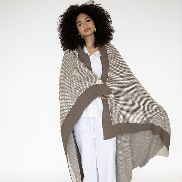 Woman wearing a beige and dark brown shawl knitted throw with a white outfit on a white background.
