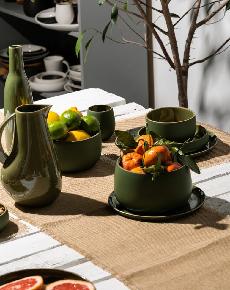 A burlap table runner with frayed edges laid across a dining table, set with dinnerware, food, and a glass of water, creating a warm and inviting dining setup.


