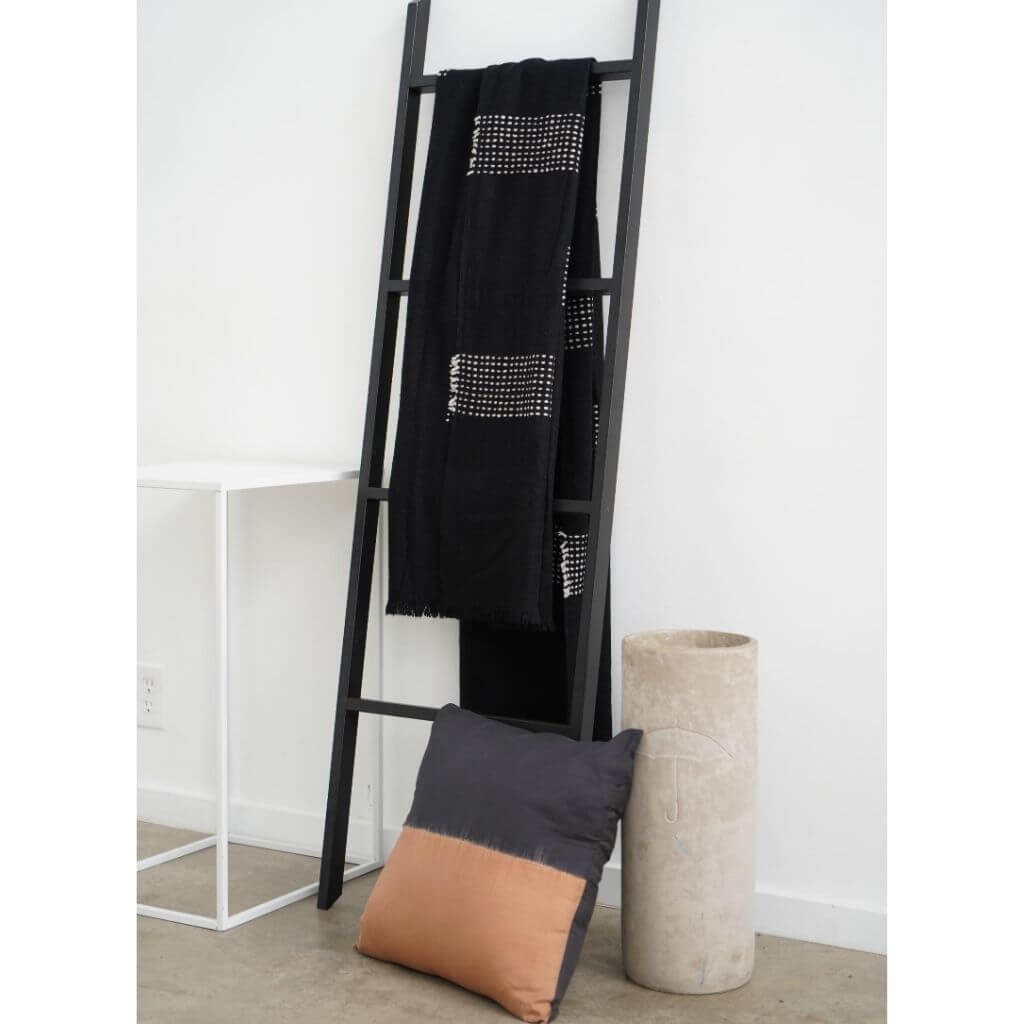 Walnut Black Yak With Hand Knotted Merino Stripes Handloom Throw displayed on a black ladder with a concrete vase and pillow.