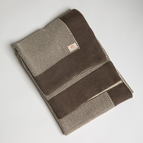 A brown and beige textured cotton throw with a dark brown border folded on a plain white background. 