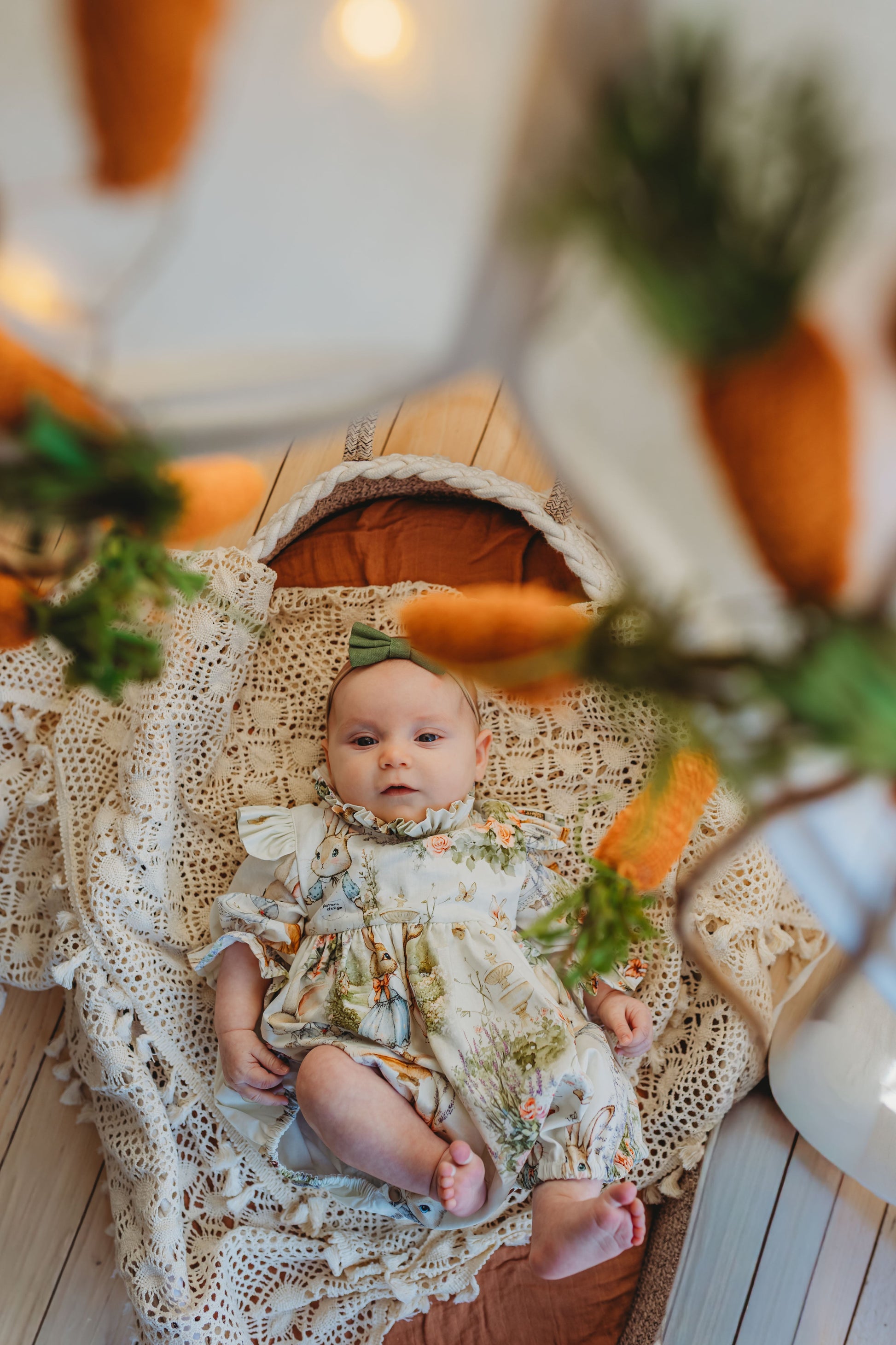 Baby in a floral dress sitting on a textured surface with pumpkins and greenery in the background