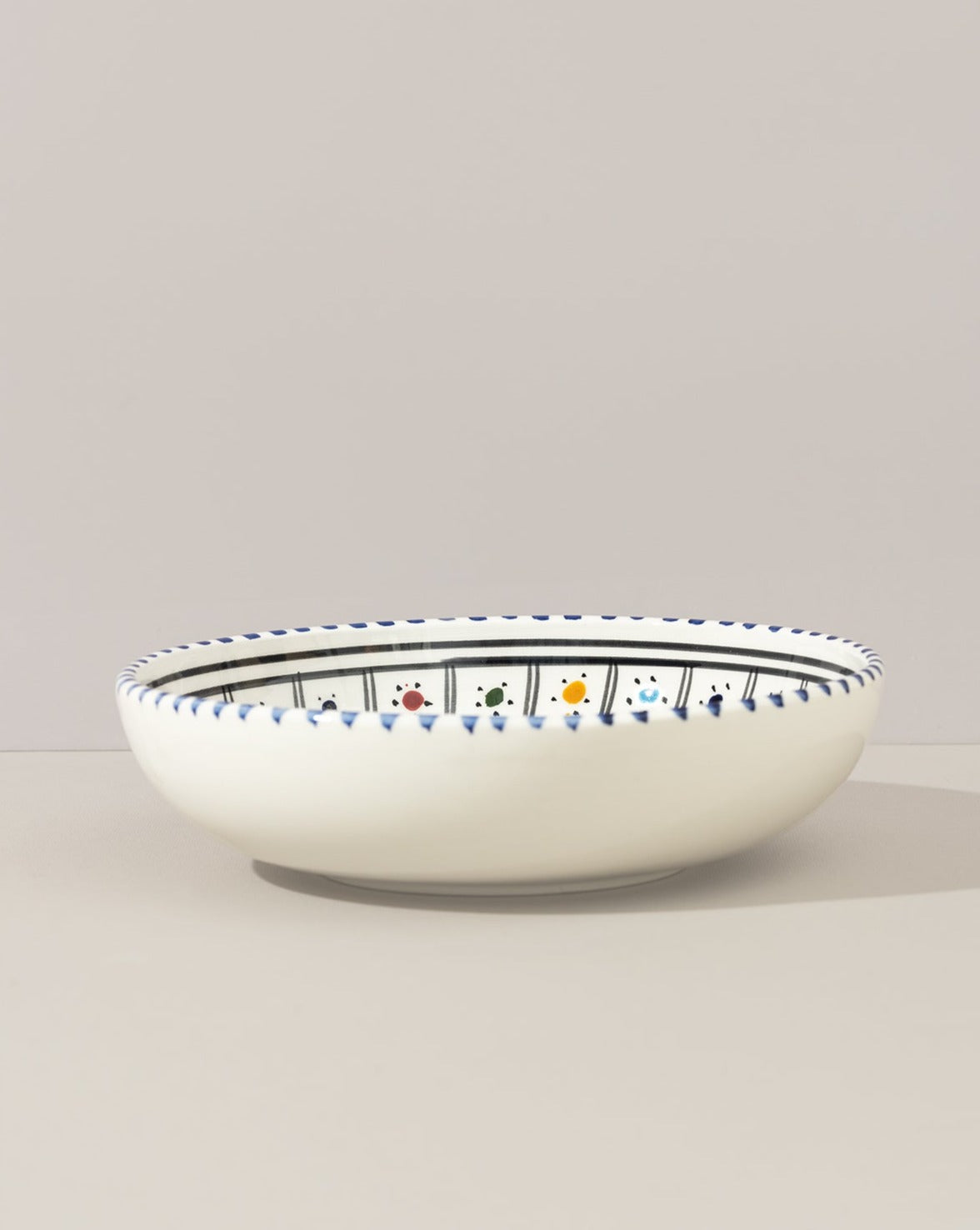 A ceramic hand painted decorative plate with a geometric pattern, predominantly white with blue and gold accents.