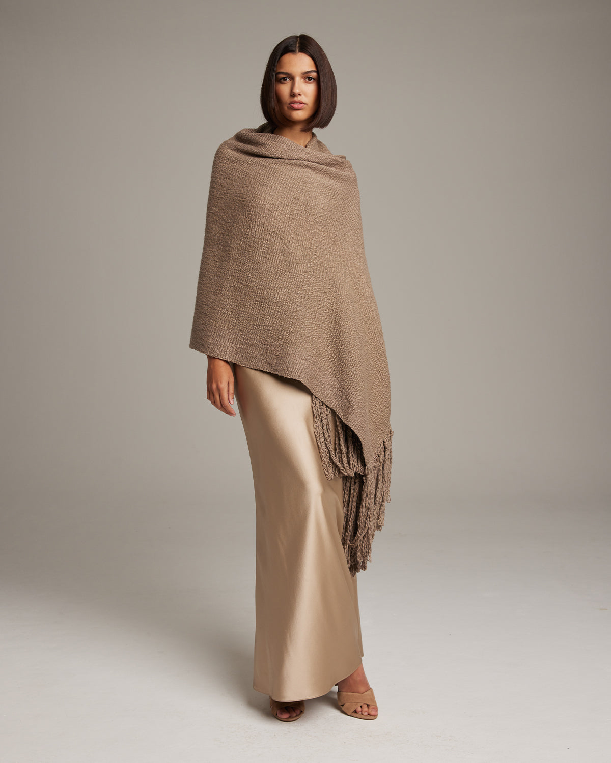 Model wearing a Flammé Fringe Wrap shawl in a neutral color, standing against a plain background.