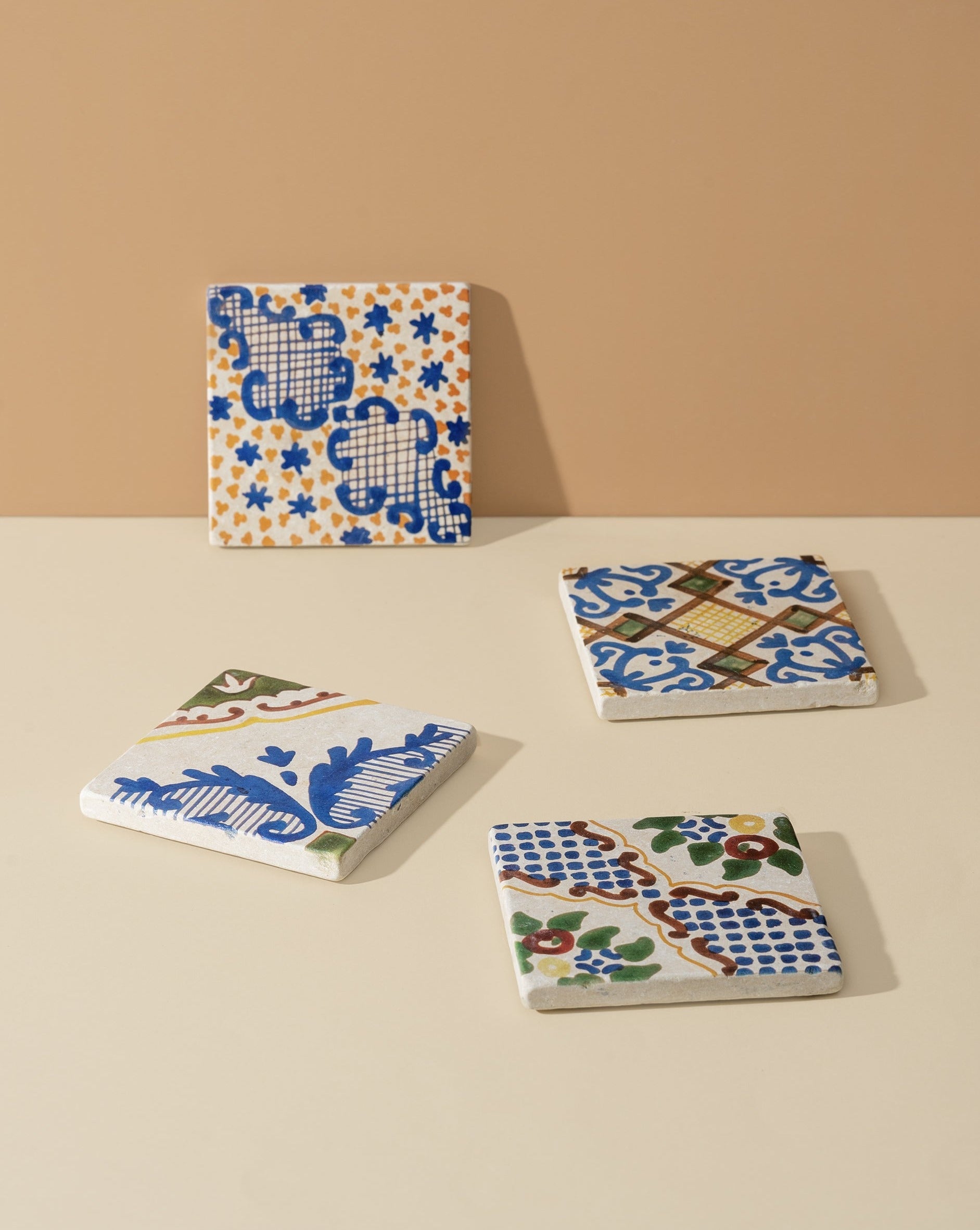 A set of four square marble coasters with hand-finished white and blue patterns, displayed on a neutral background.