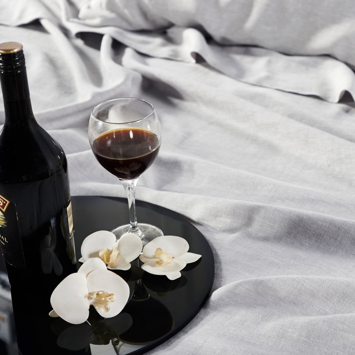 CSS-516-7284_4|Luxurious light grey 100% linen sheets provide a comfortable backdrop for a drink and orchids, enhancing bedroom elegance.
