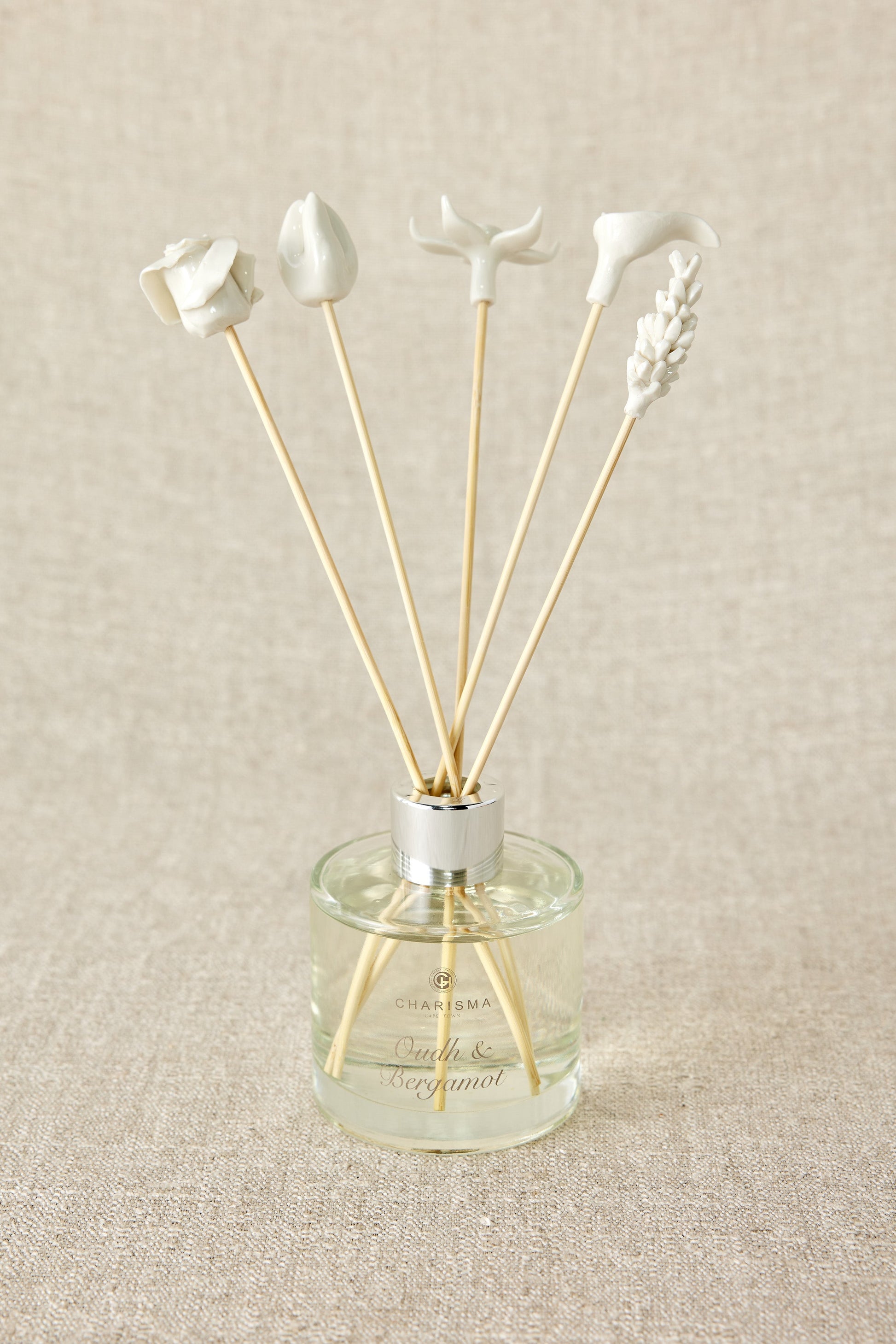 A set of white porcelain floral diffuser sticks placed in a clear glass container, with a beige background.