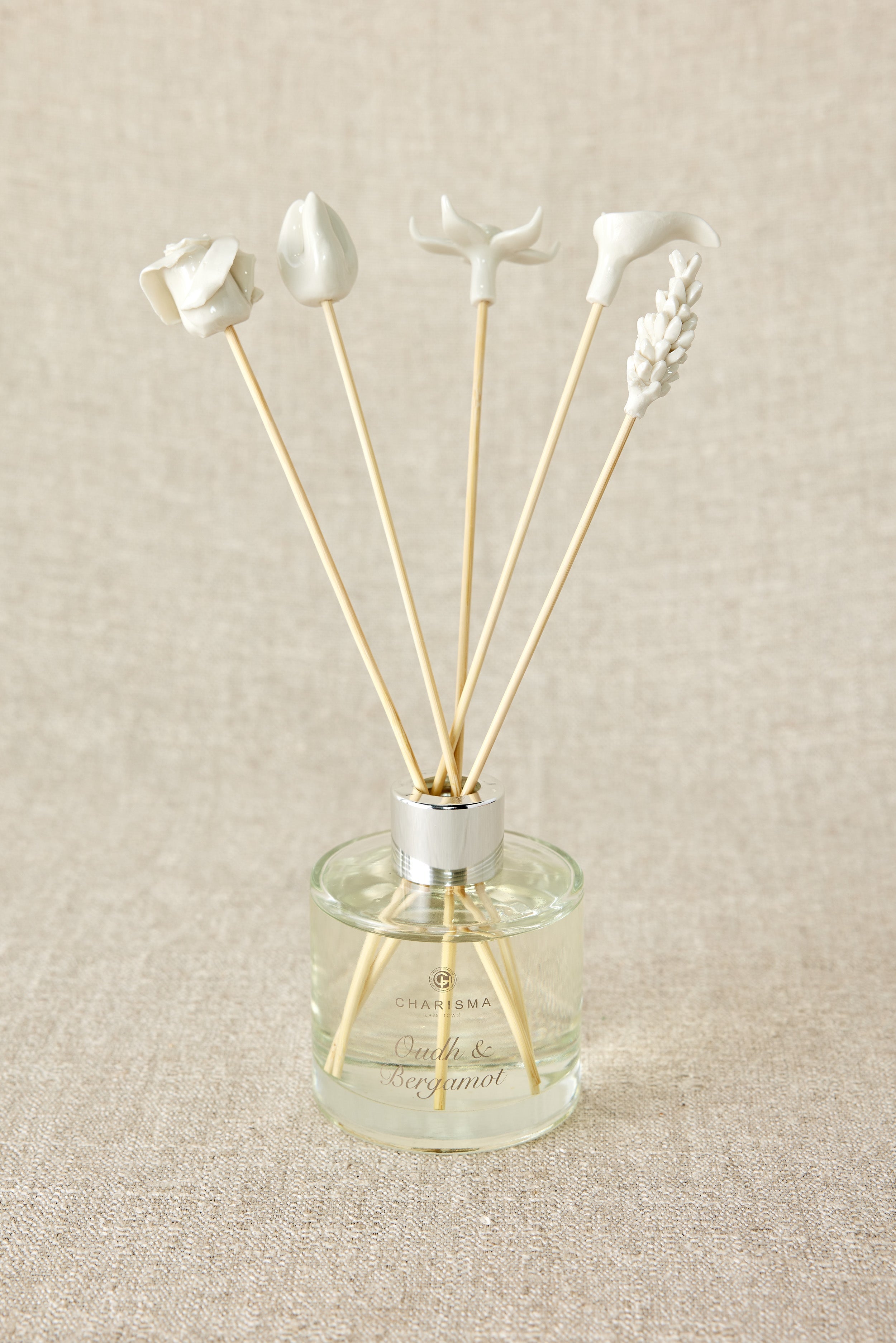 A set of white porcelain floral diffuser sticks placed in a clear glass container, with a beige background.