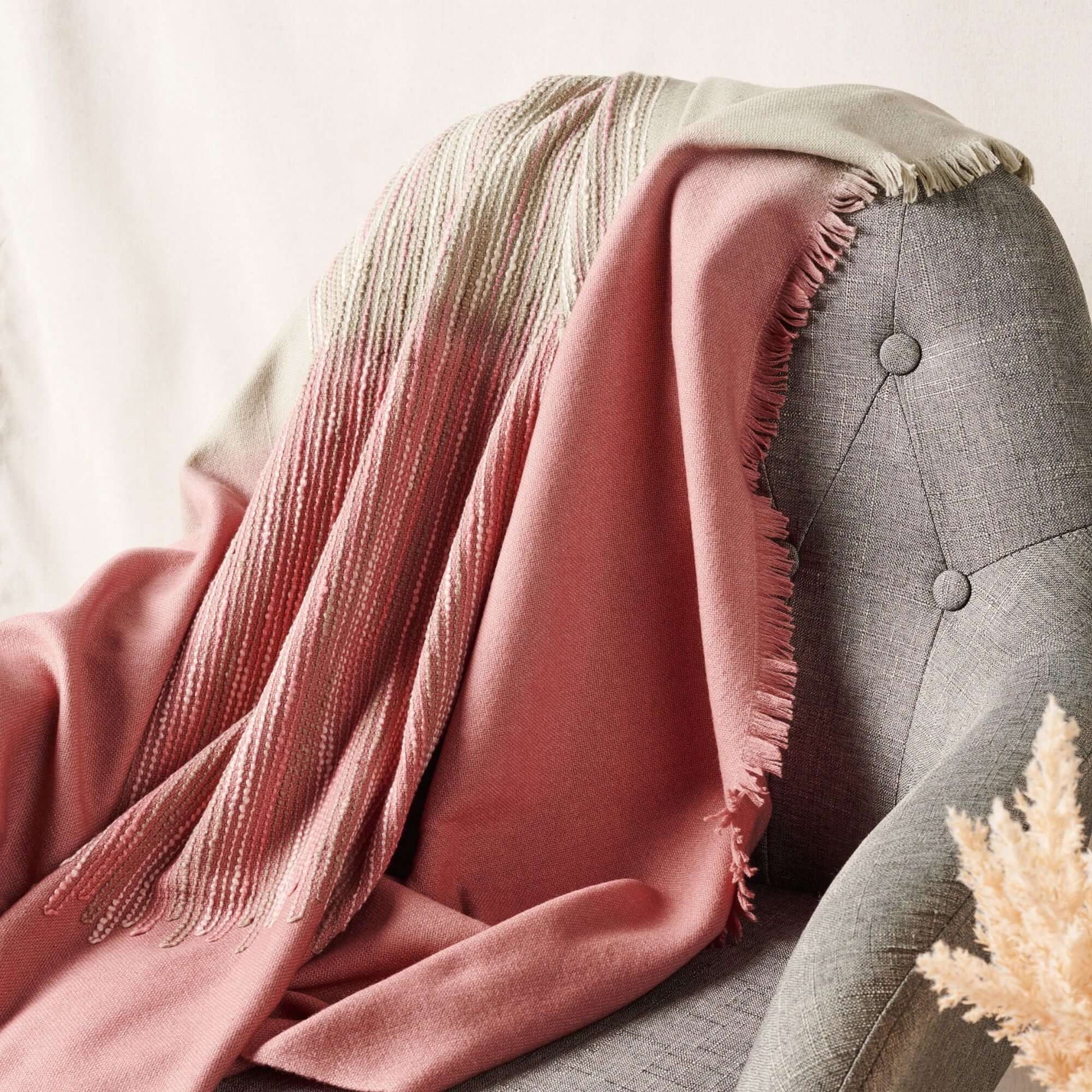 Chive Pink Green Ombre Handloom Merino Throw draped over a gray armchair showcasing its unique colors and textures.