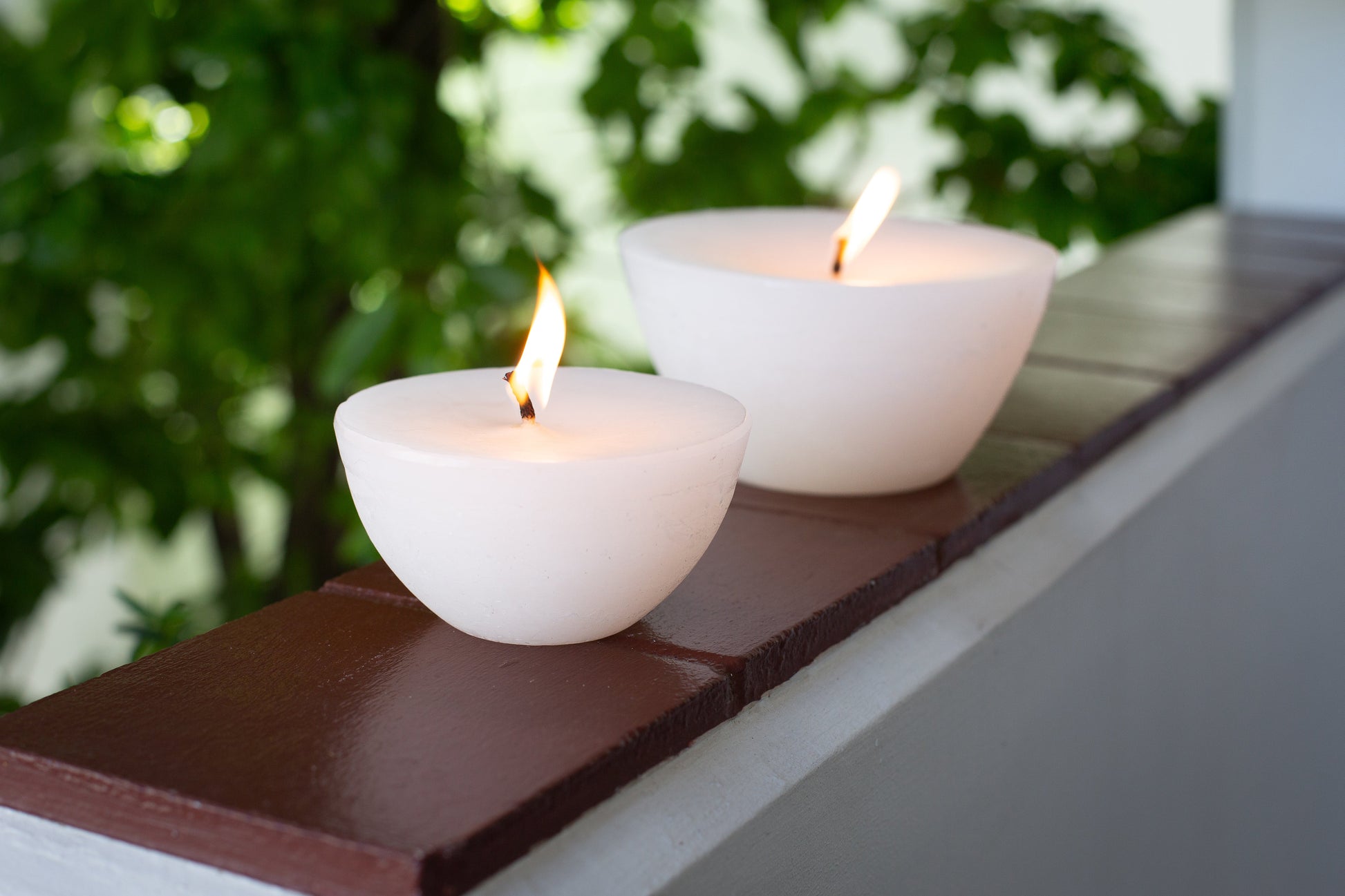The two Luma Afrika Outdoor Bowls sitting on a ledge outside to show the difference scale. Infused with citronella & lavender to repell insects. 