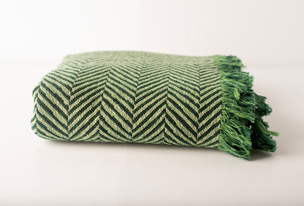 Front view of folded green and cream herringbone woven cotton throw on a white background