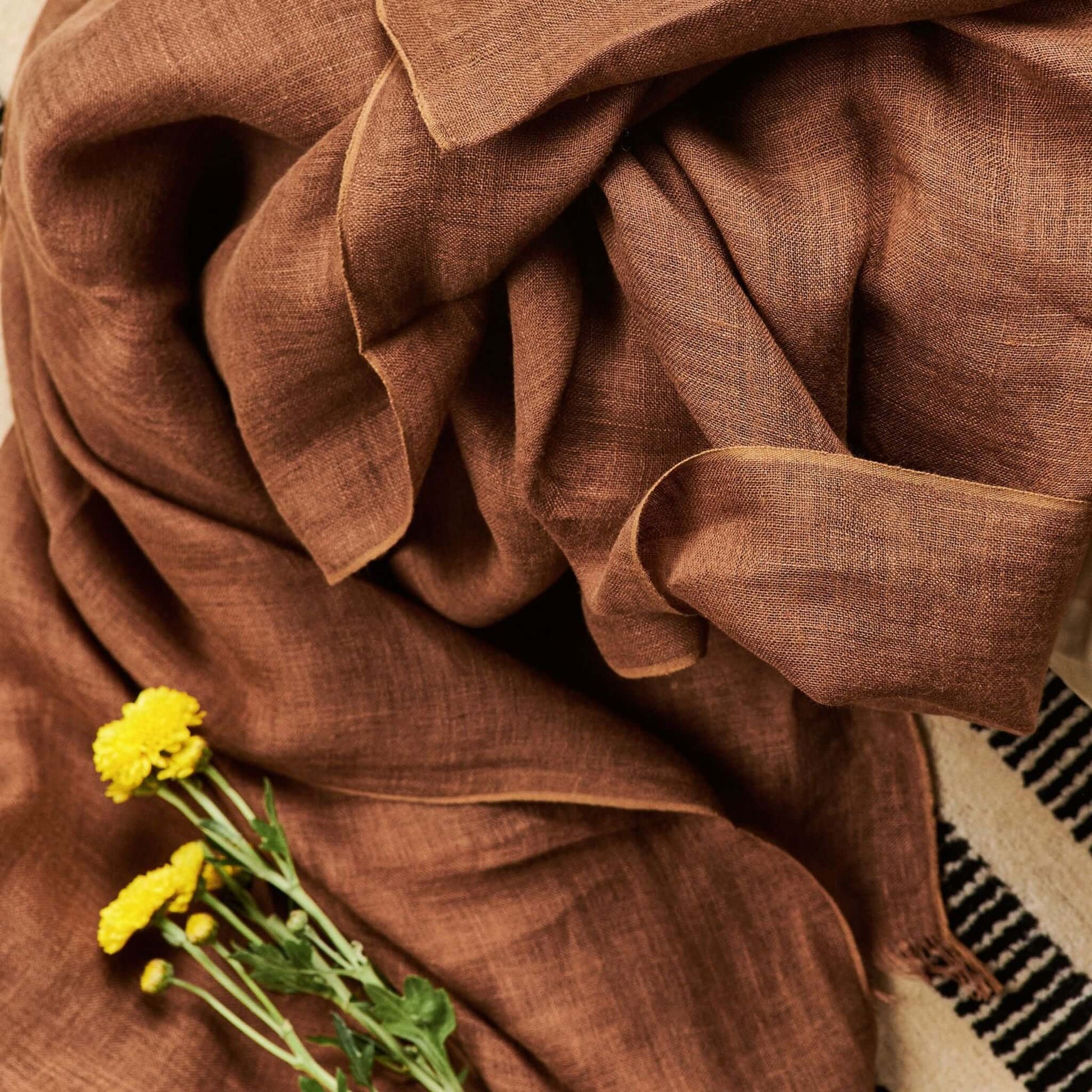 Coco Brown Hand Woven Linen Silk Blend Scarf draped elegantly with yellow flowers.