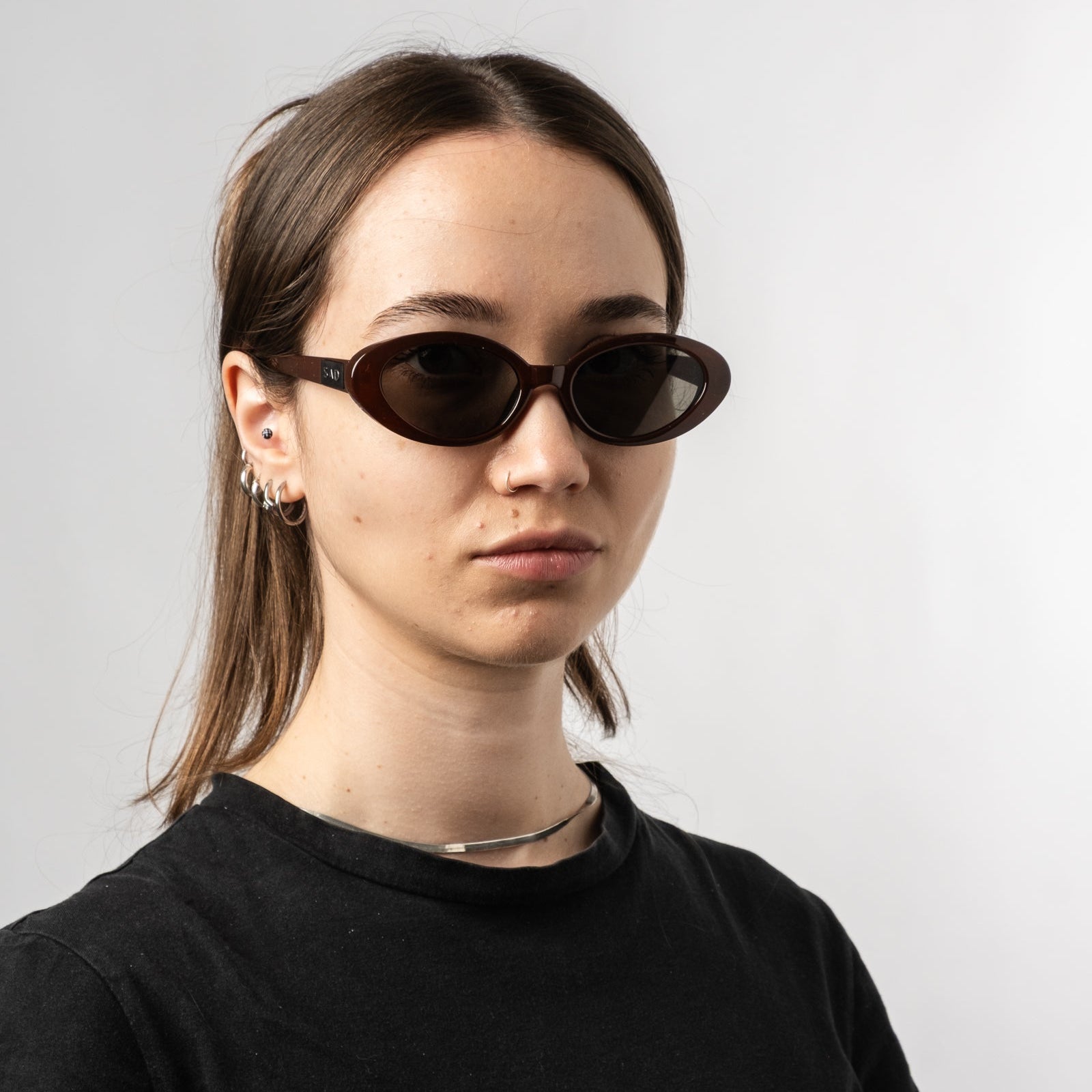 Female wearing Sad Eyewear Bloom oval sunglasses in tobacco red with tinted black lenses
