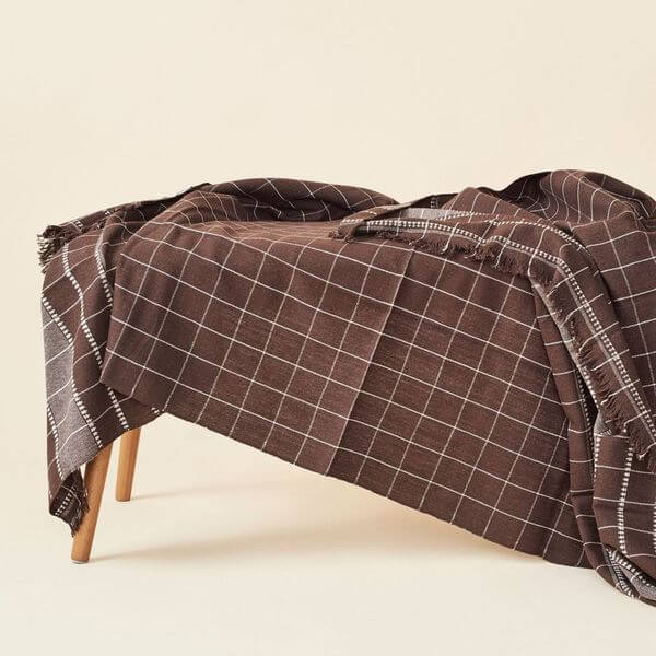 Treacle Checks Pattern Organic Cotton Handloom Throw draped elegantly on a wooden bench.