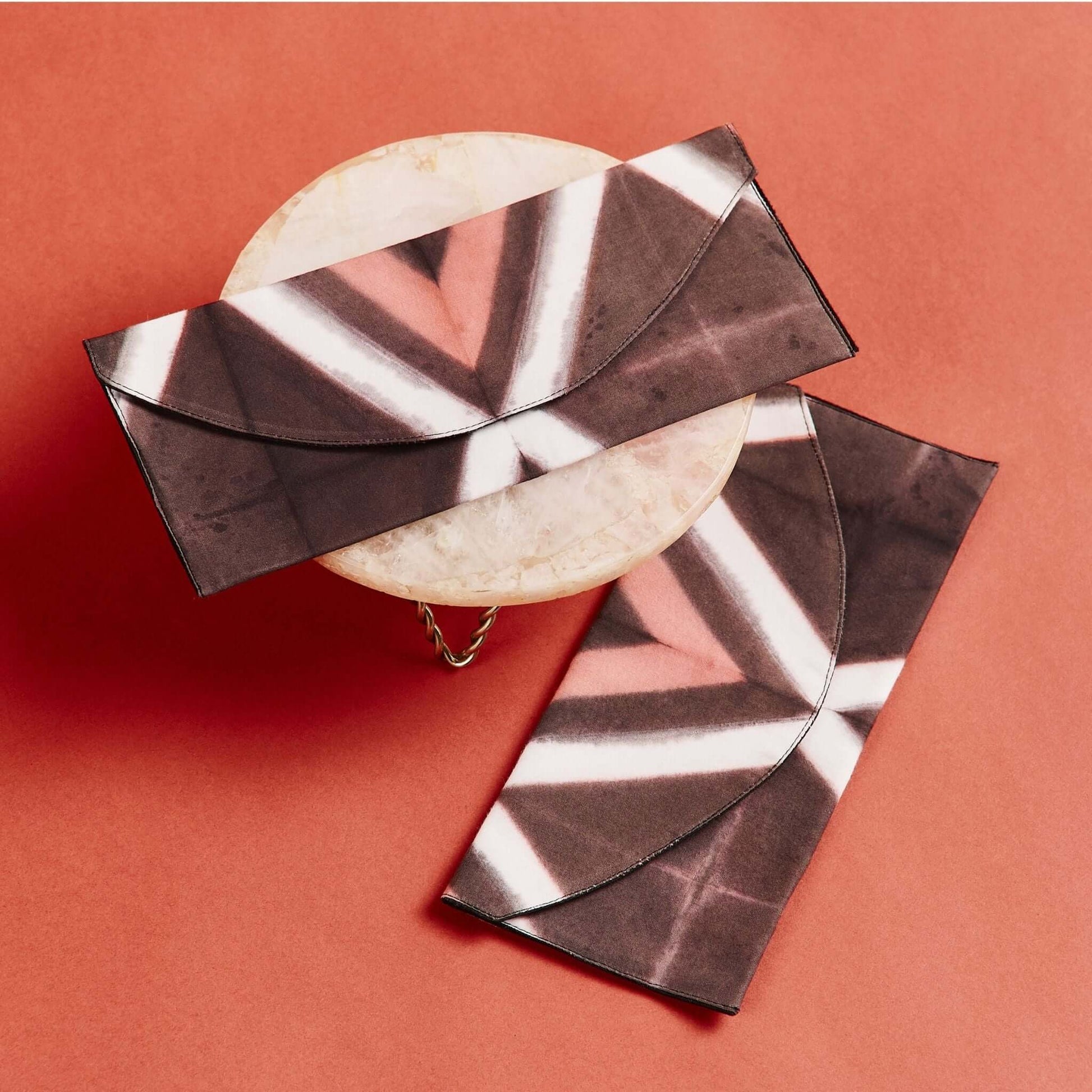Tisa Artisanal Pouch In Black Pink Triangle Print displayed on a round marble surface against a coral background.