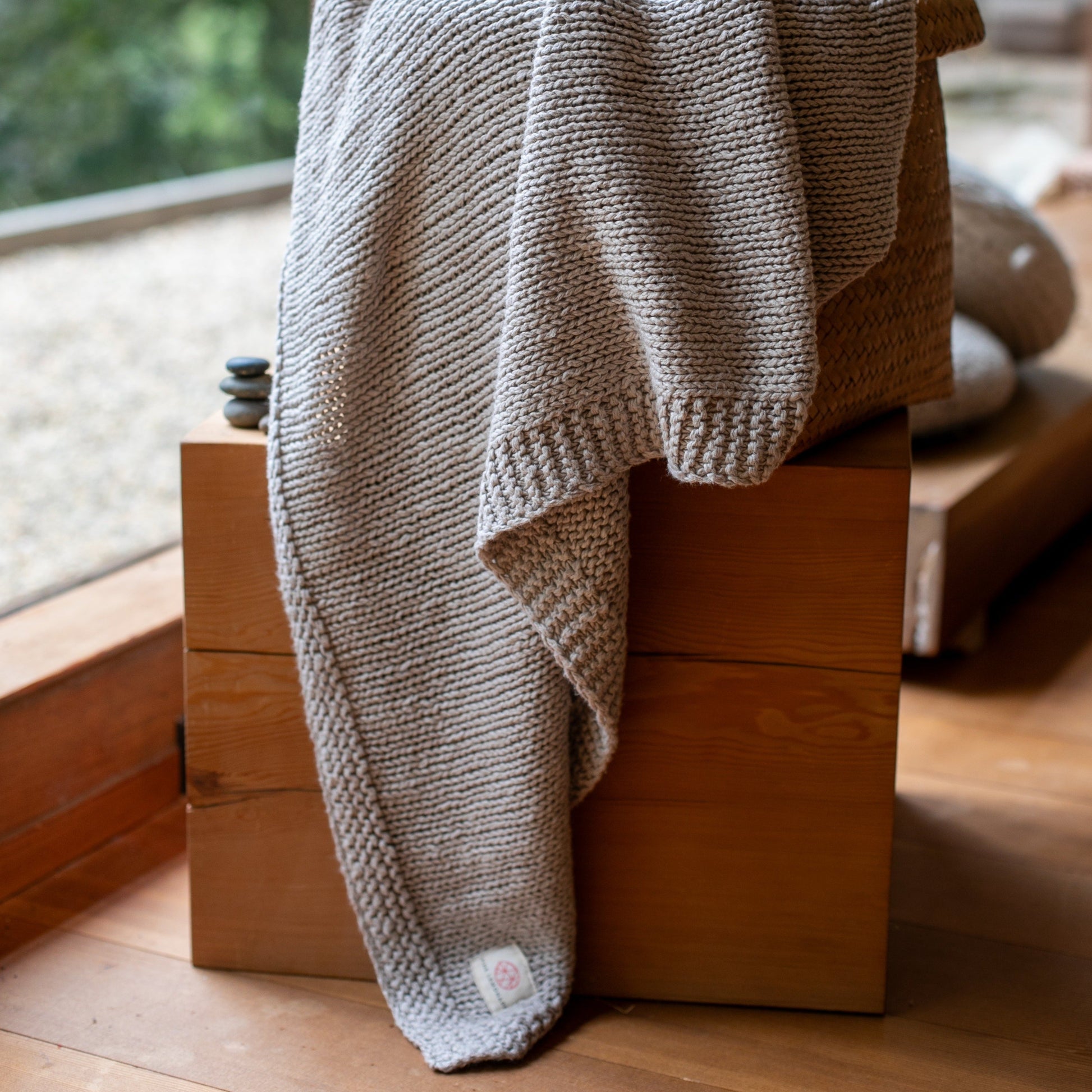 Stone grey knitted throw blanket hanging on top of a wooden box.