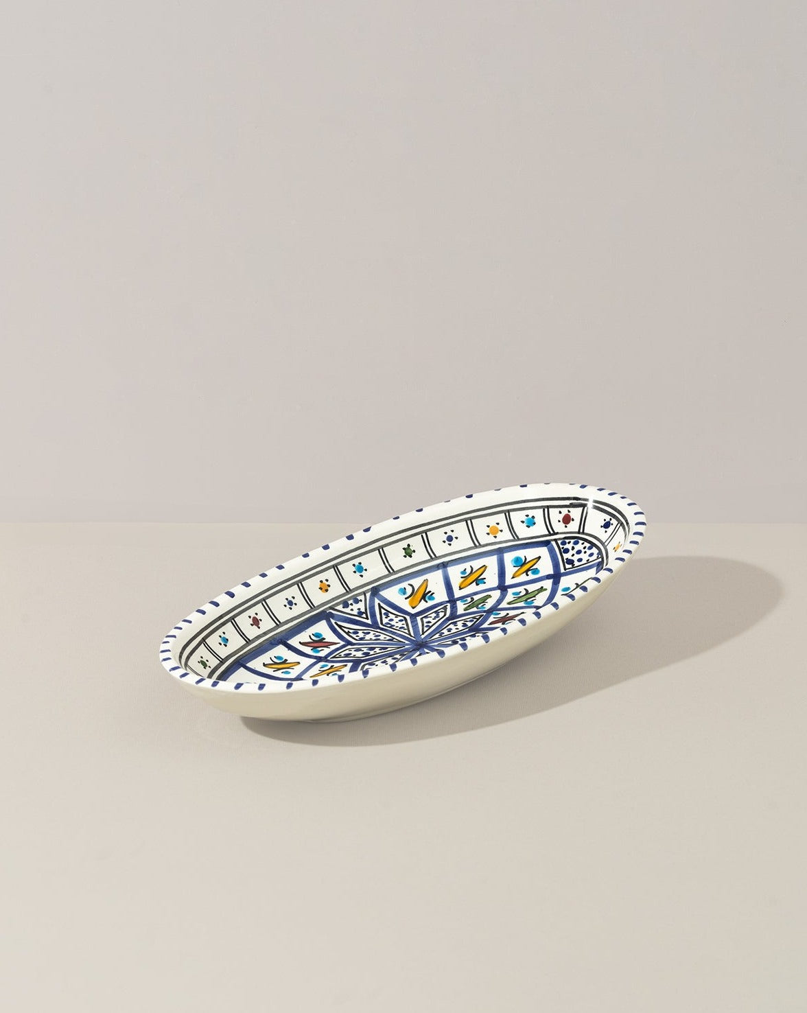 A hand painted decorative oval ceramic plate with a geometric pattern, predominantly white with blue and gold accents.
