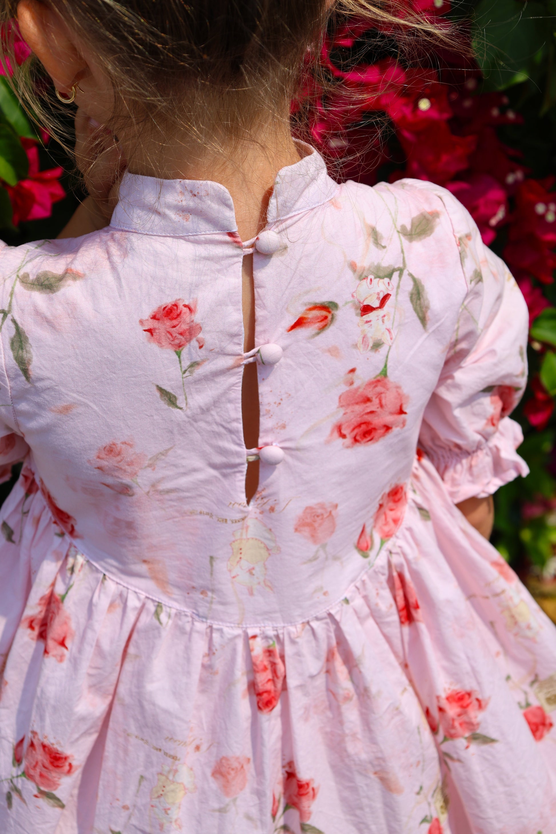 Close-up of a person wearing a floral dress with pink flowers and green leaves against a blurred floral background.