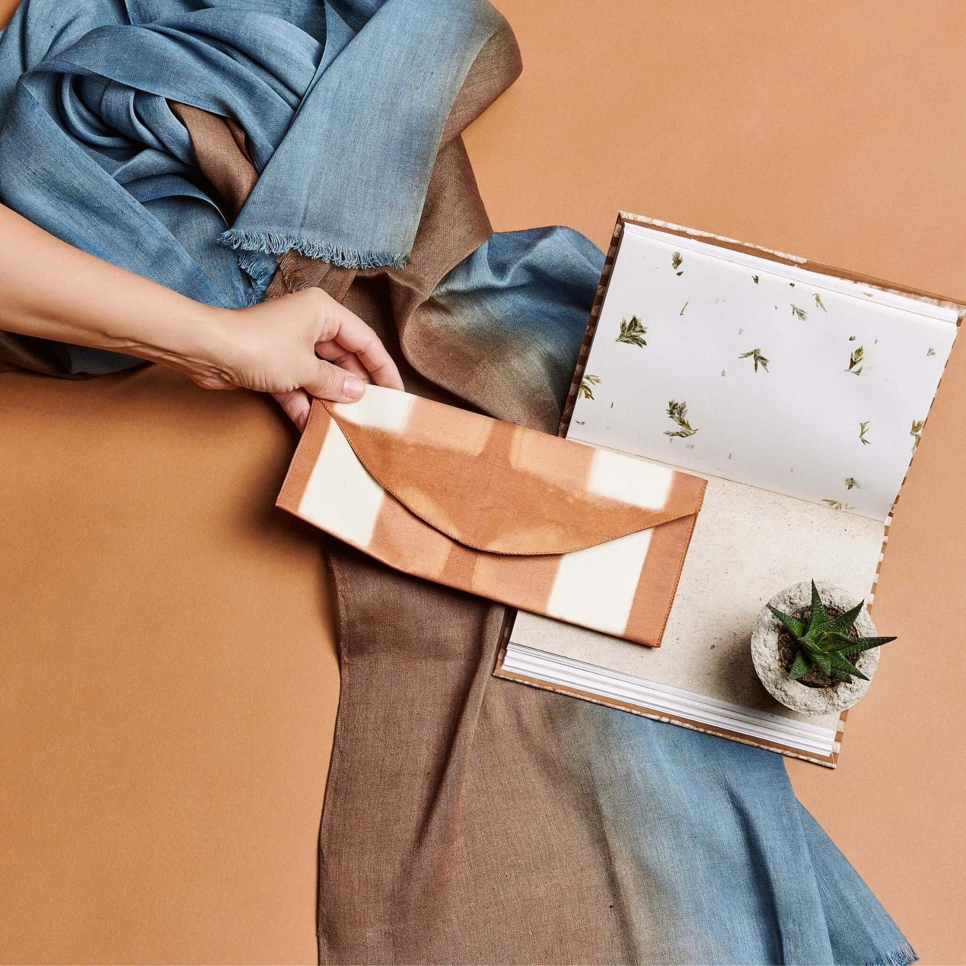 Melo Gold Mulberry Silk Shibori Hand Crafted Envelope Pouch held with a scarf and a notebook in the background.