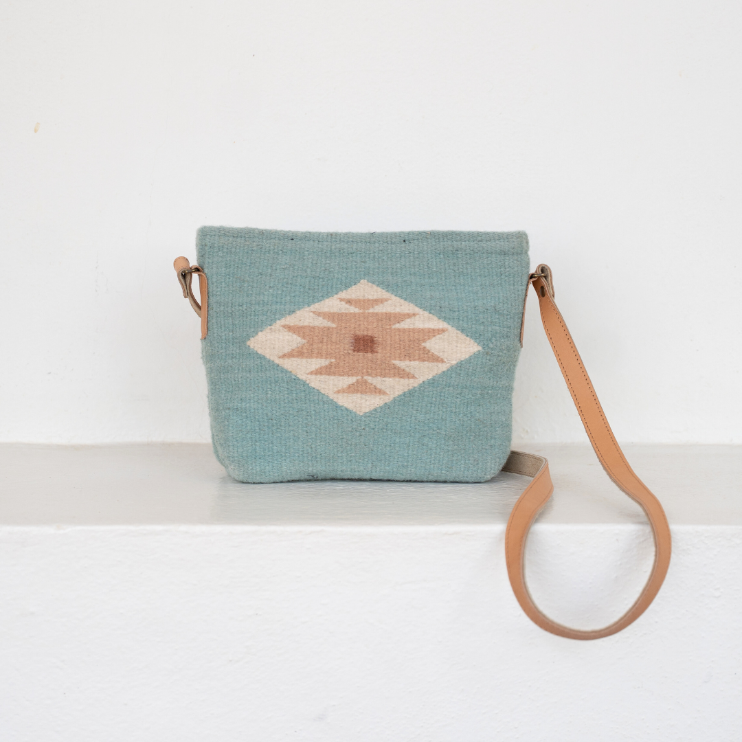Woman carrying handwoven crossbody bag with minimalist Zapotec butterfly design in soft blue tones; features adjustable leather strap and two internal pockets for daily essentials