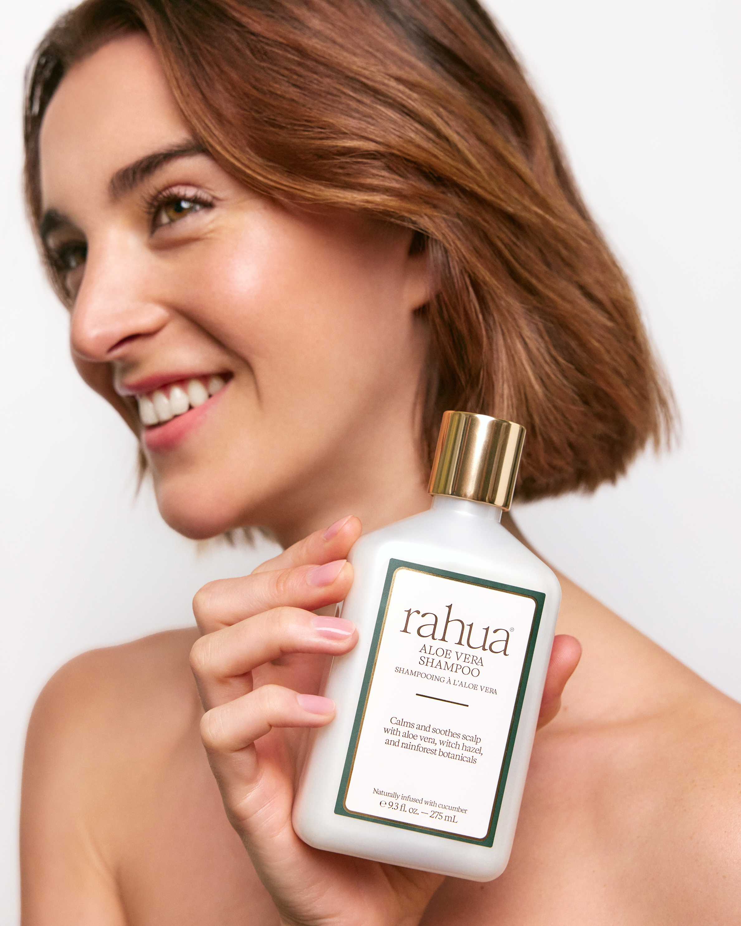 Woman holding a bottle of rahua aloe vera body lotion against a white background