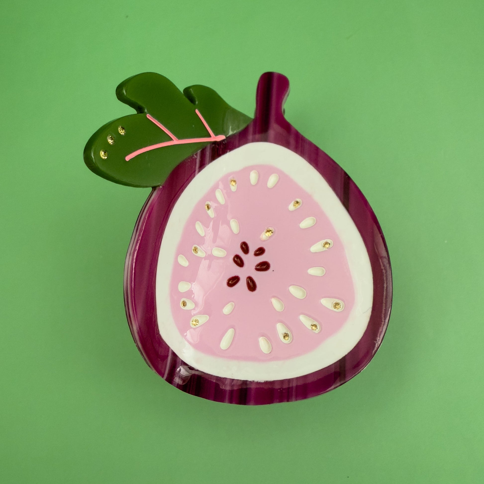 Decorative hair claw like a sliced fig on a green background. 