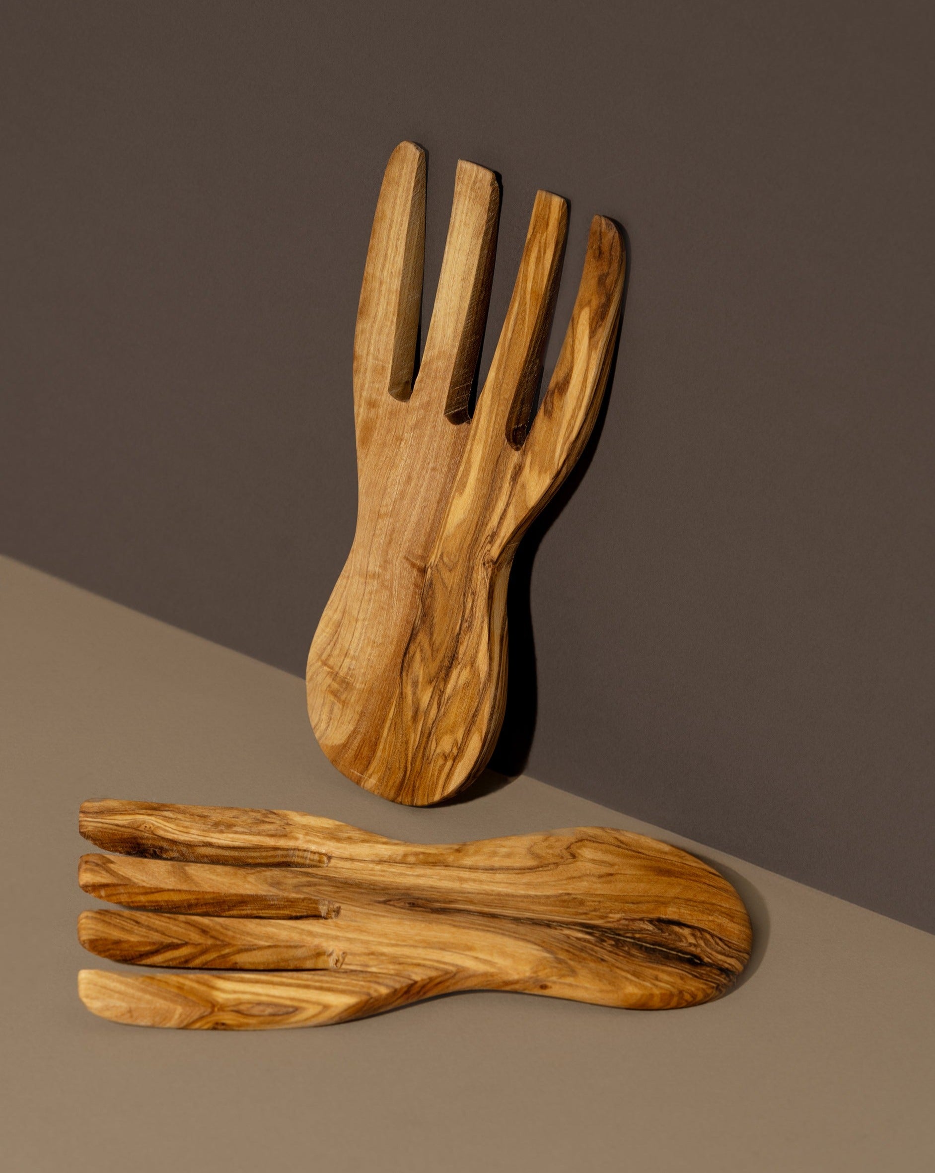 A pair of flat olivewood serving forks placed on a dark surface.