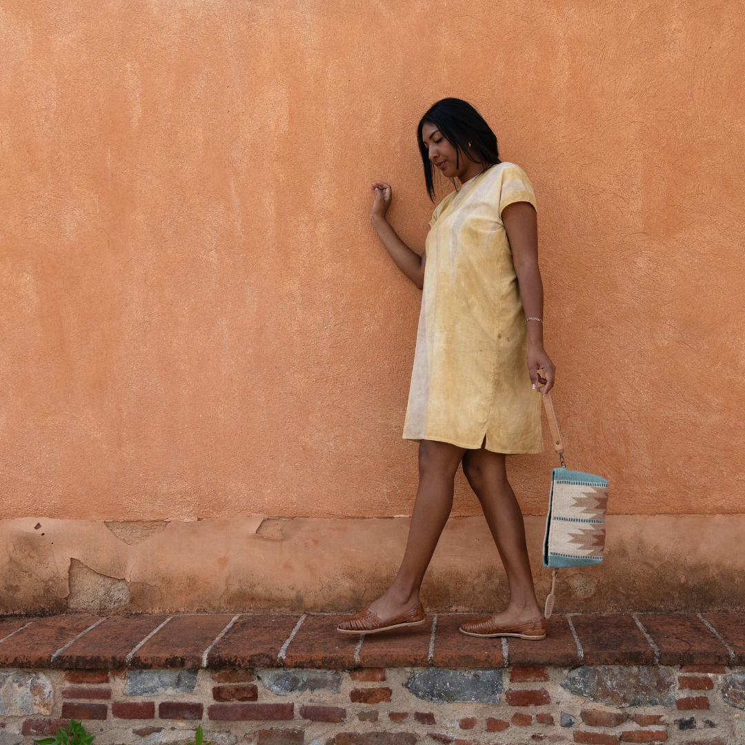Woman wearing handwoven convertible clutch with Zapotec lightning design in rose and blue tones; functions as a pouch, wristlet, or crossbody with leather straps and internal pocket