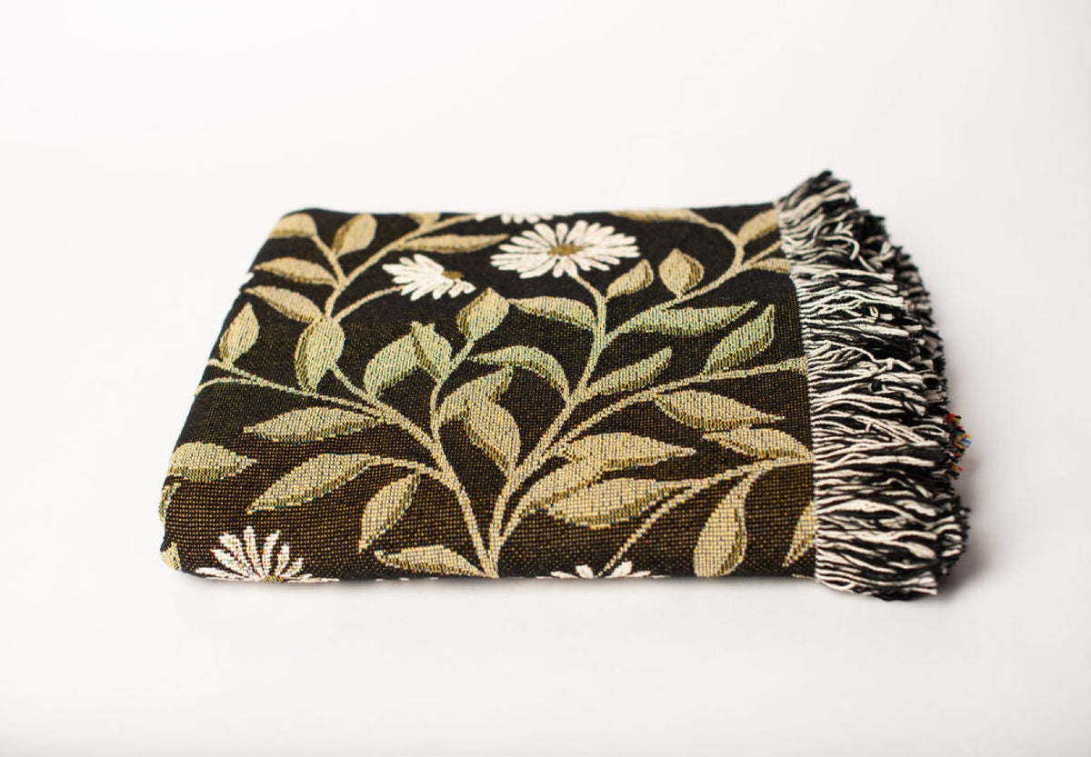 Close-up of May Bramble black, gold, green, and cream floral botanical jacquard woven blanket with fringe