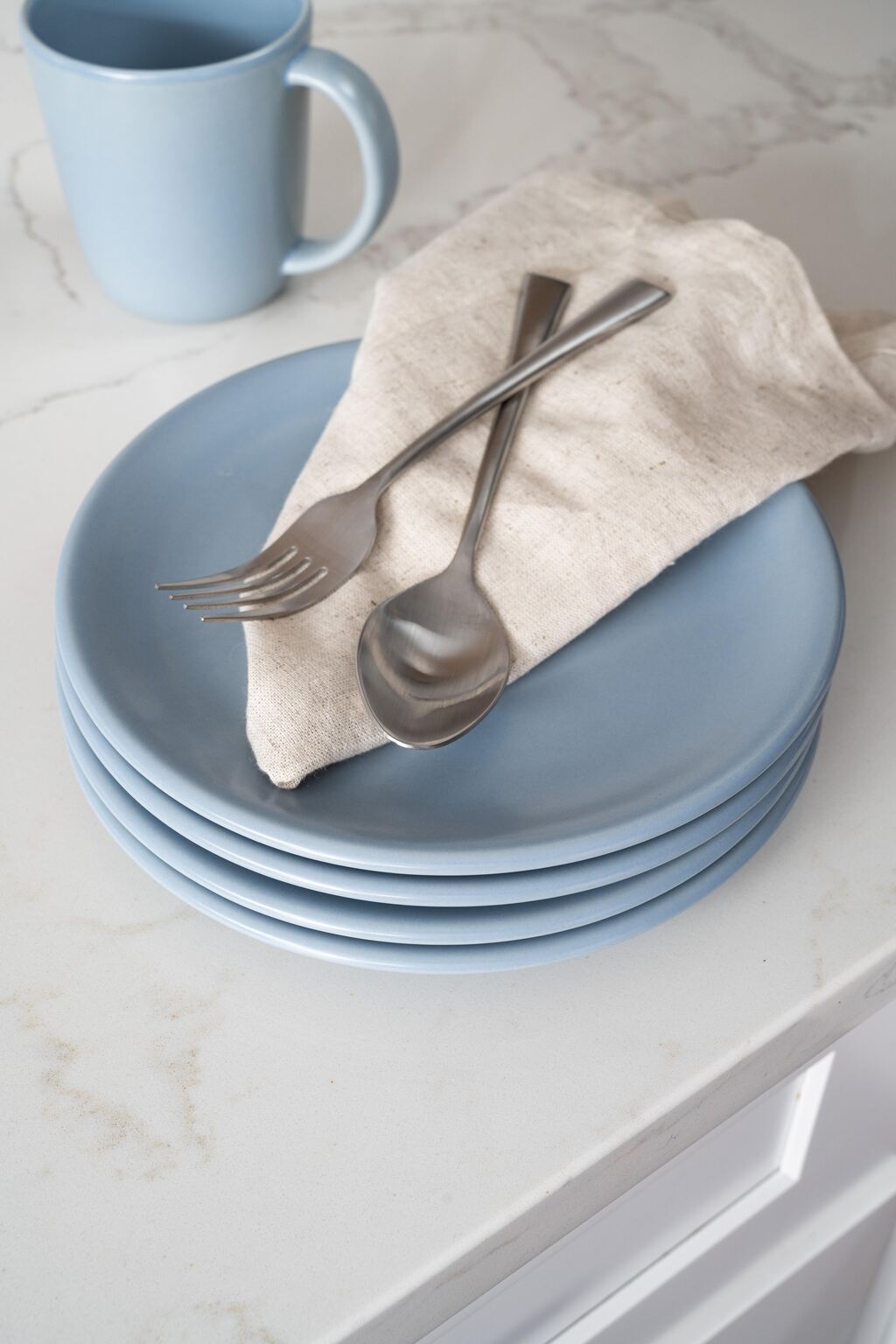 Stacked Wave blue Petite Plates by Hamkke Home with linen napkin and stainless-steel flatware on a marble countertop.